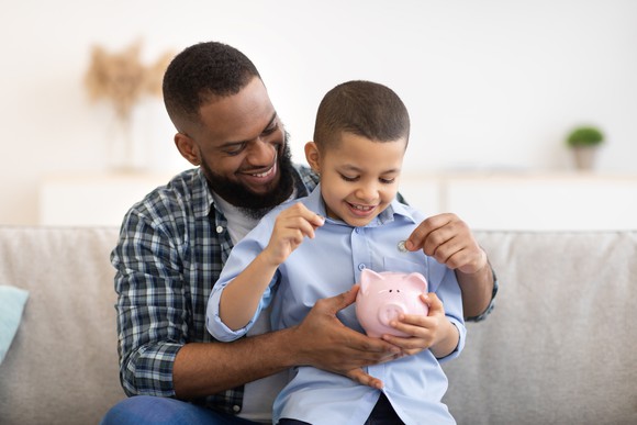 Parent and child adding money to piggy bank. 