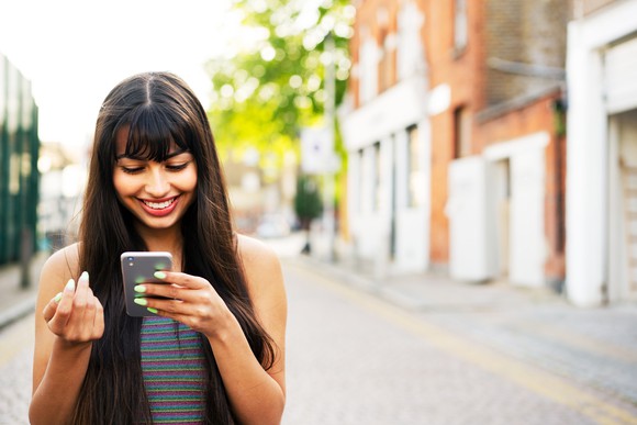 Person on the street, looking at a phone, smiling. 