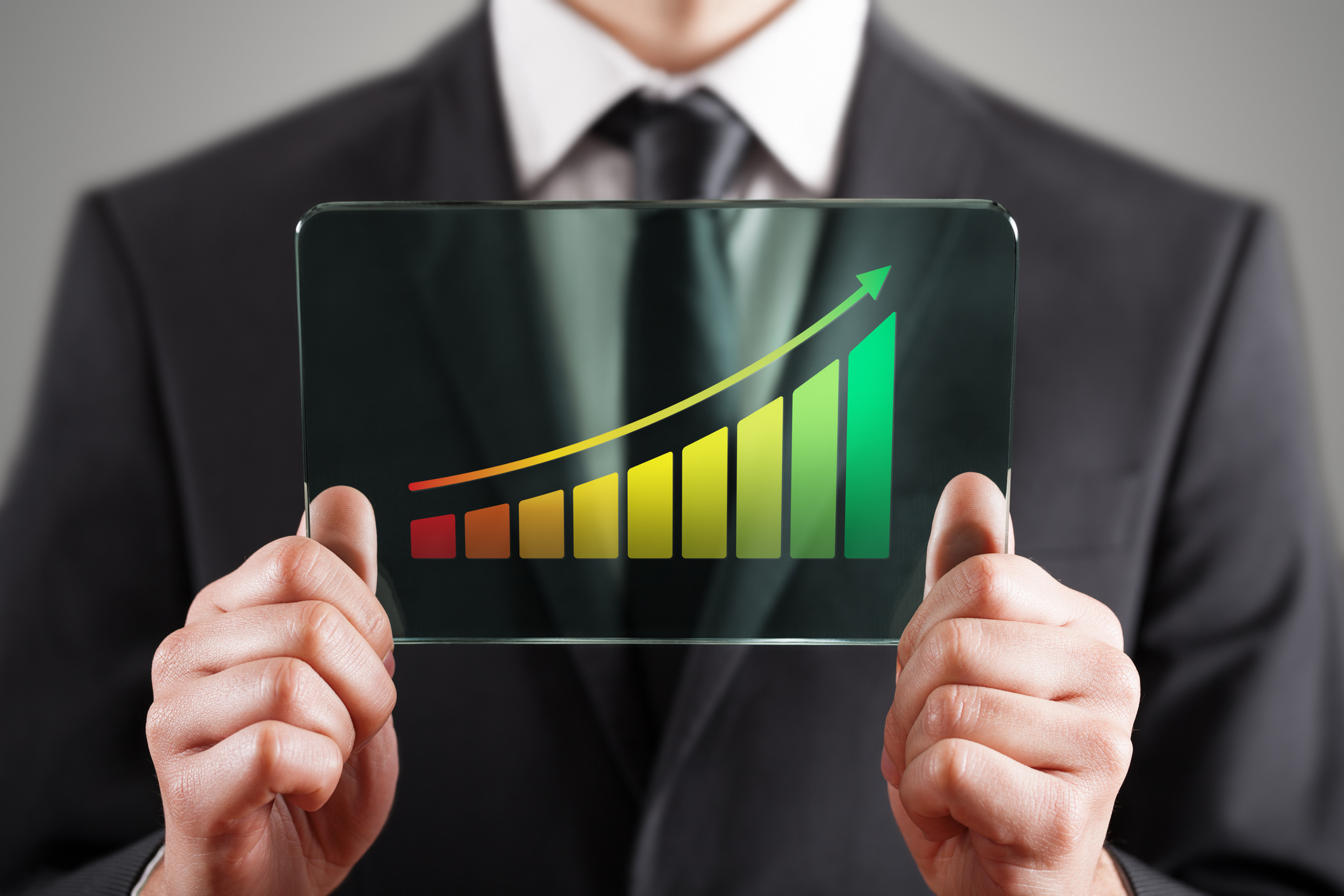 Person in suit holding a glass screen that shows an upward trending bar chart.