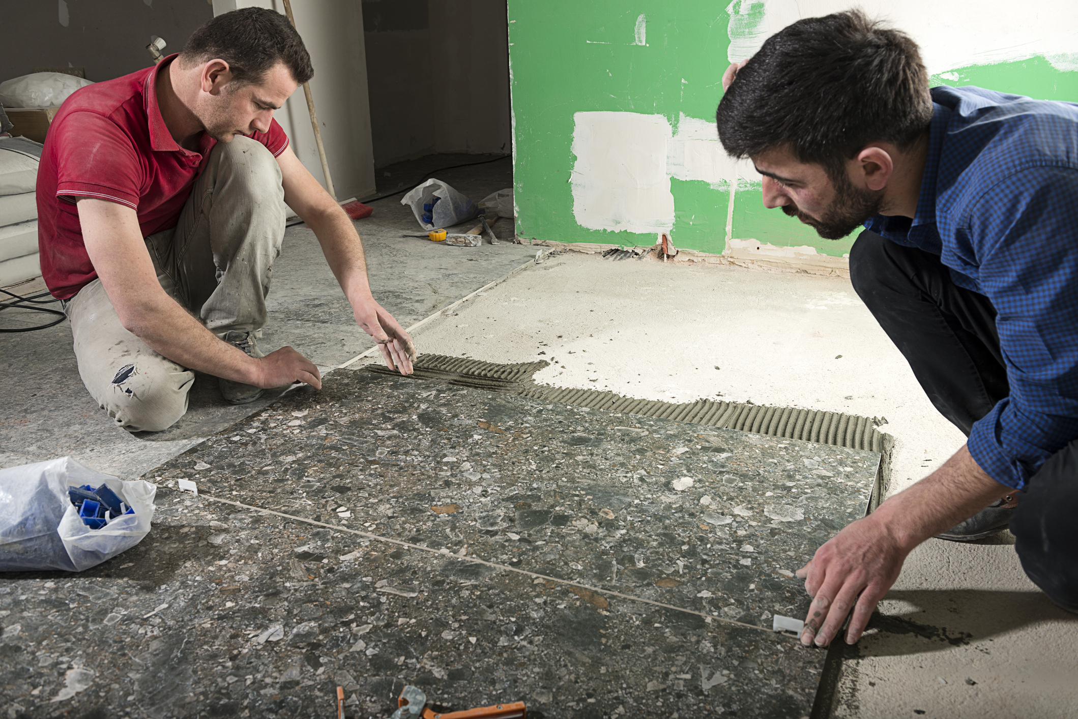Two people install tile floor.