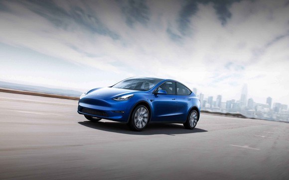 A blue Tesla Model Y cruises down an open freeway.
