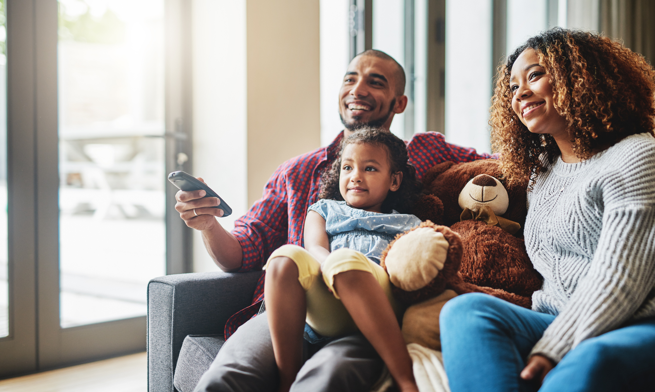 A family sitting on a couch with a remote control in hand.