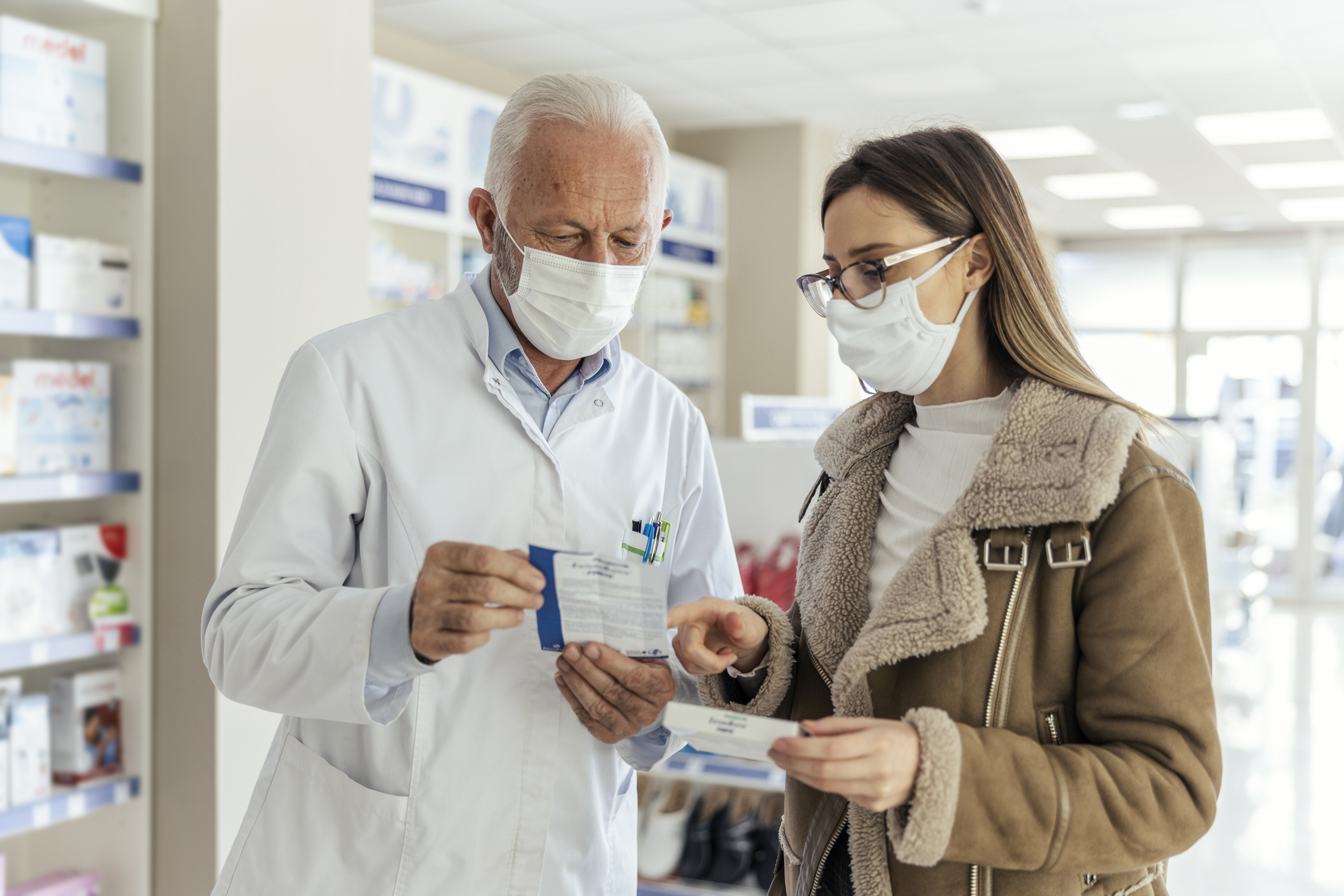 Pharmacist and customer wearing masks discussing a prescription.