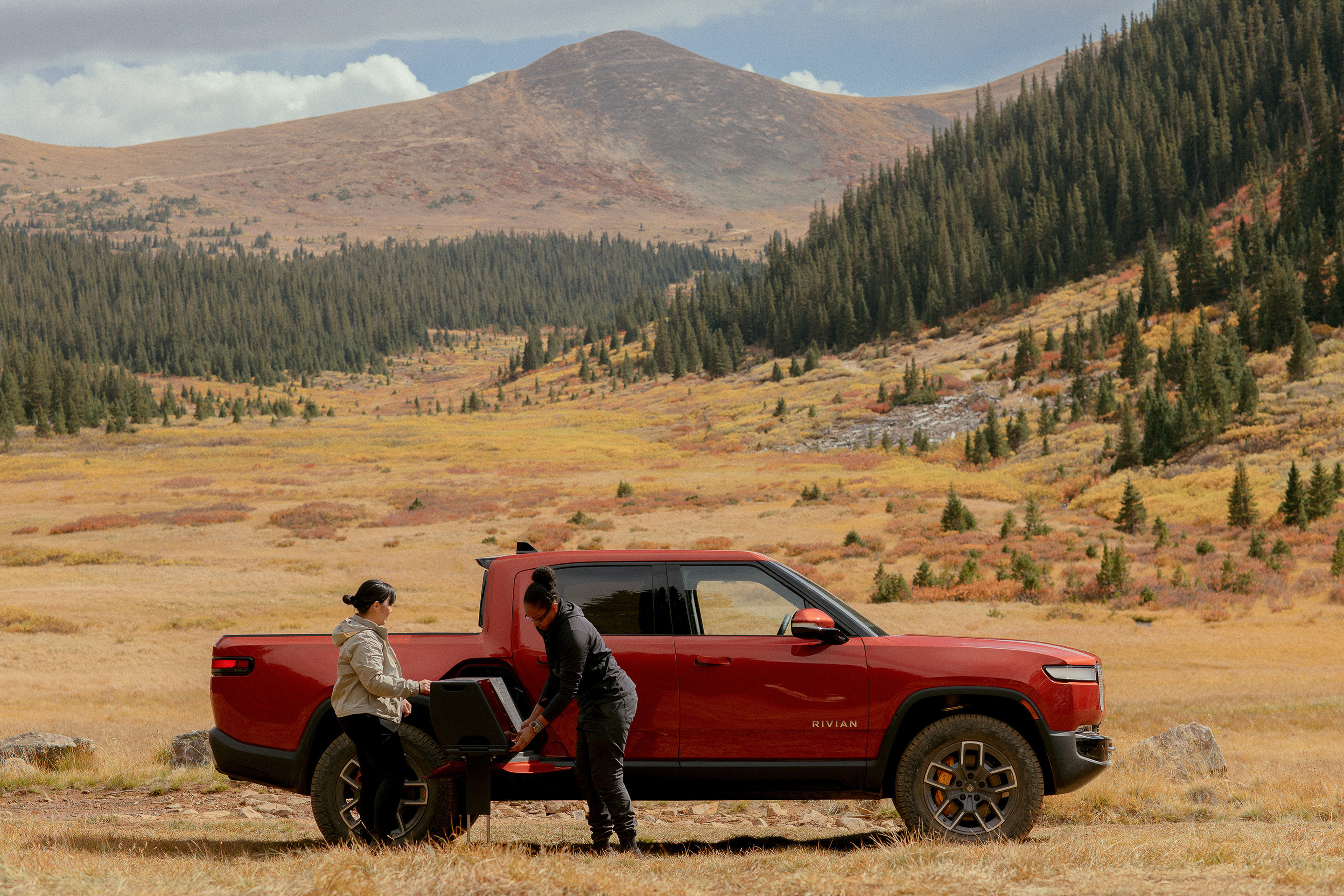 Rivian R1T pickup truck in the wilderness with two owners. 