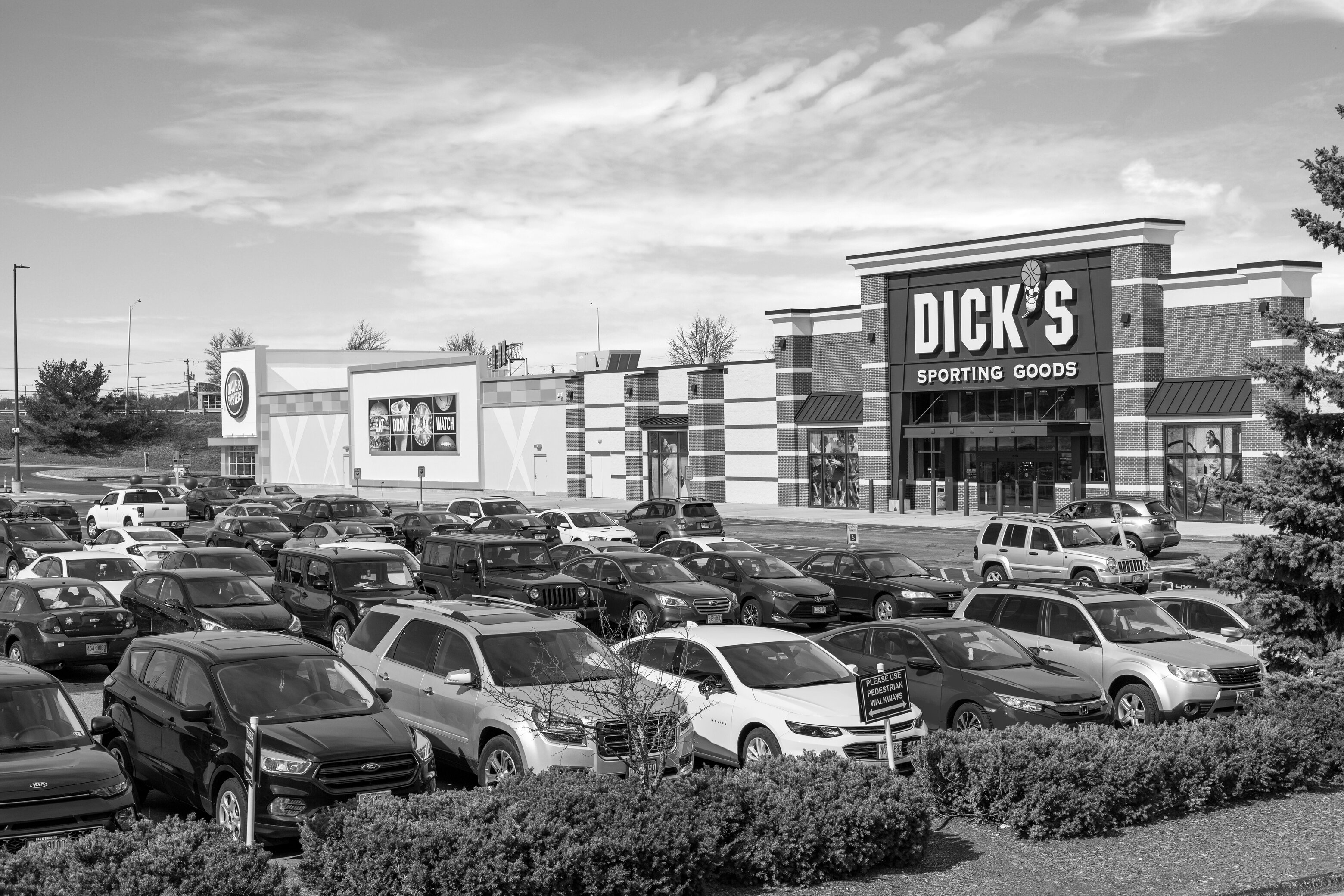 A black-and-white photo of cars in the parking lot outside a Seritage shopping center.