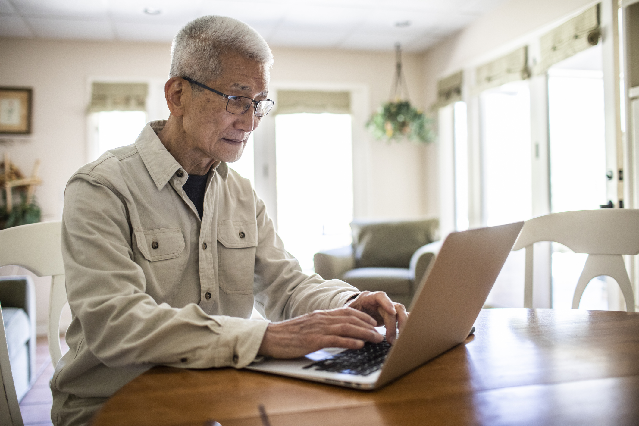 Older adult typing on laptop.