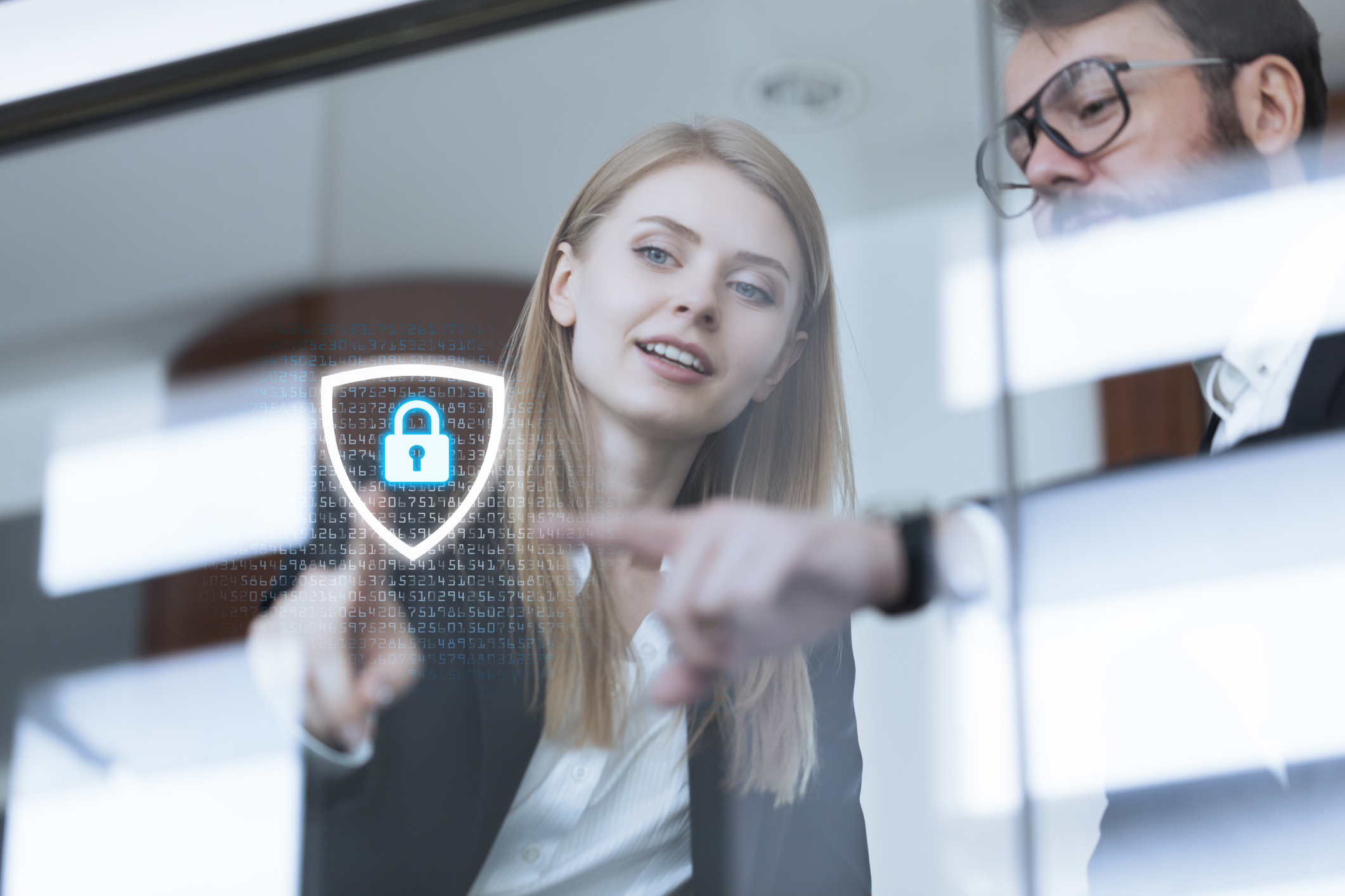 Two young business people work with data on a screen showing a lock security icon.