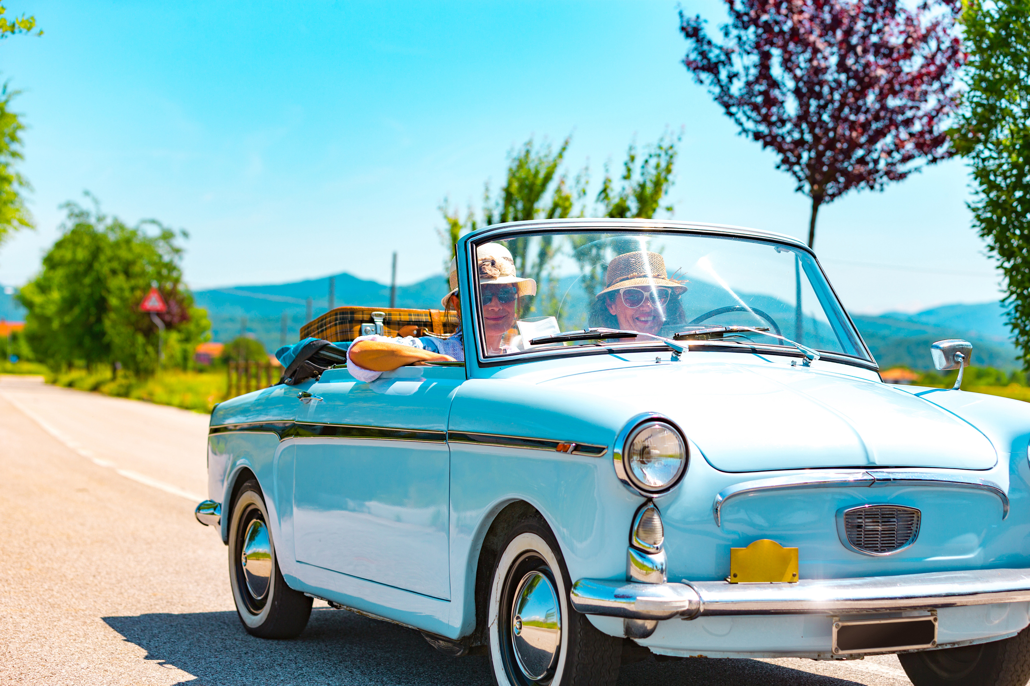 Two people driving in a vintage car.