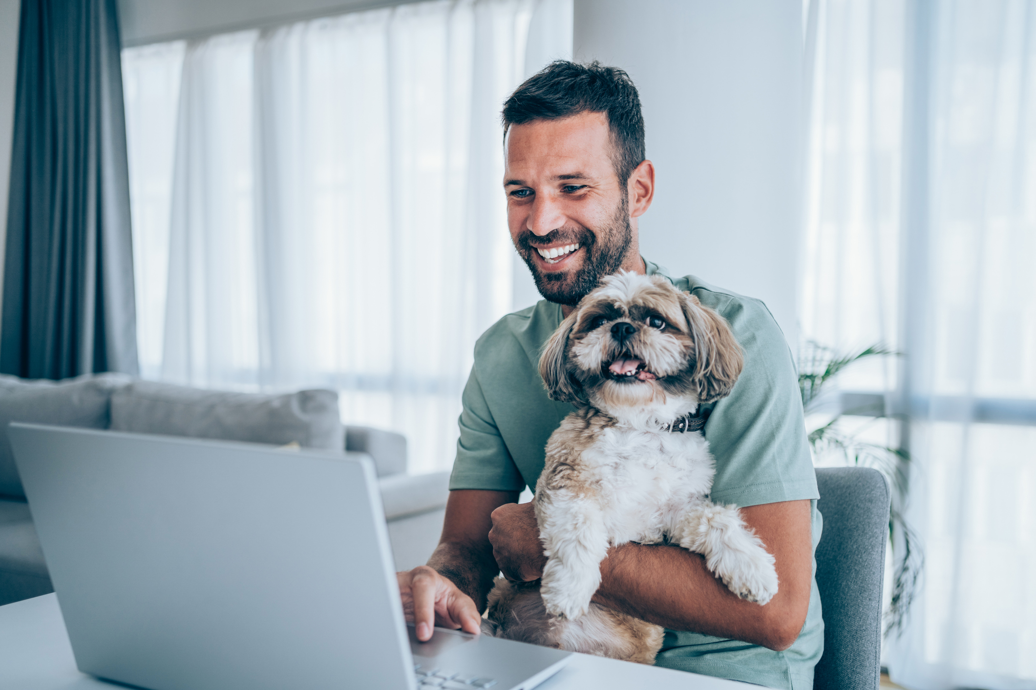 A smiling person at a laptop holding a dog.