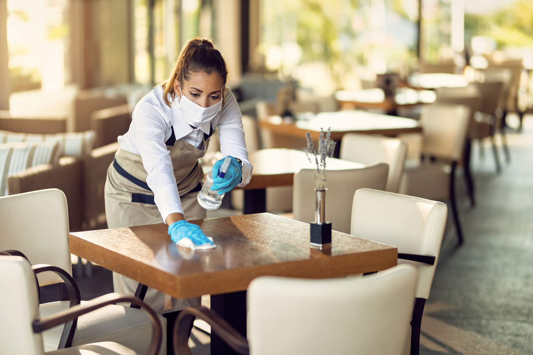 A person in gloves and a mask cleaning a restaurant table.