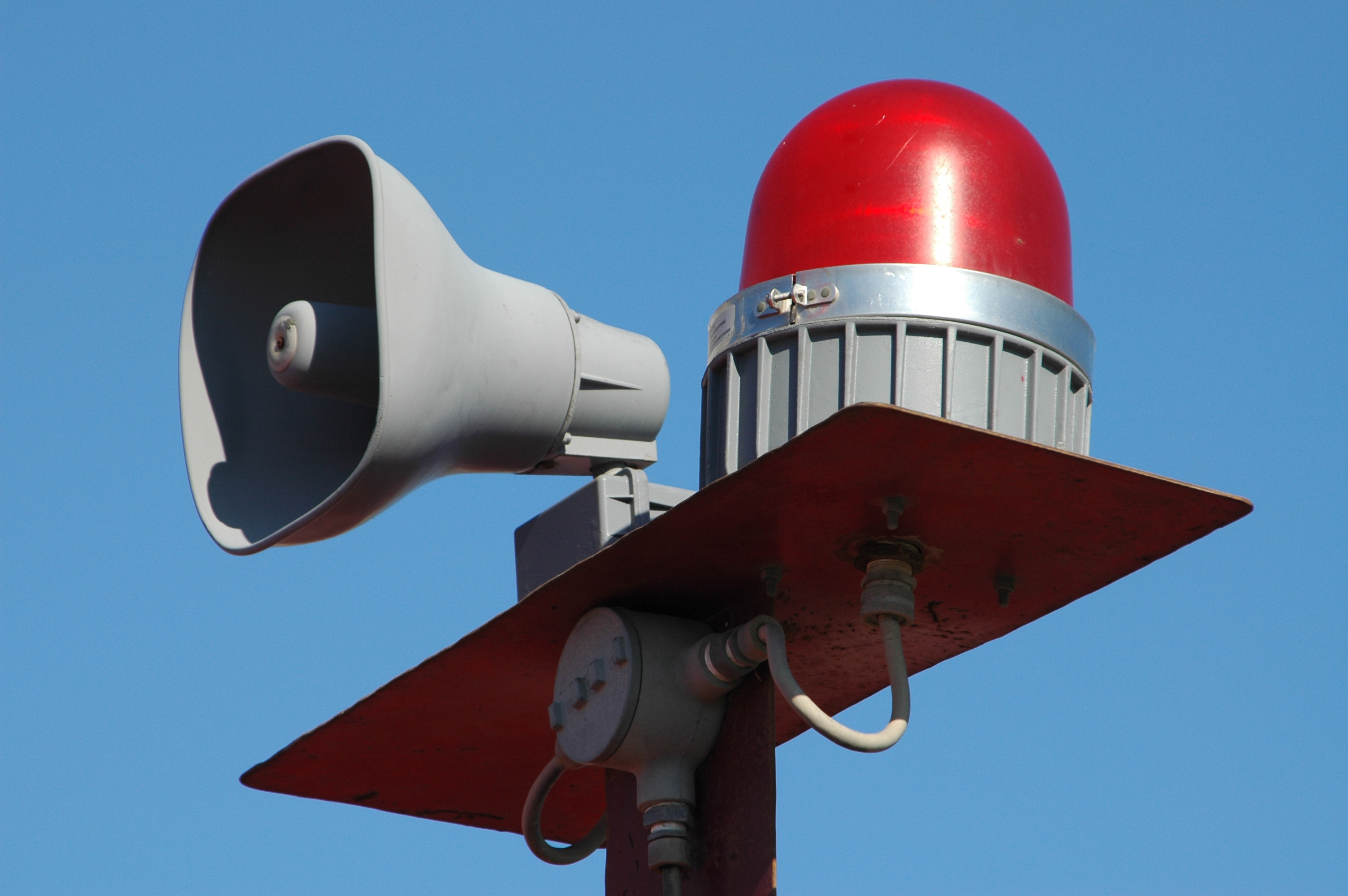 A siren and a signal on a lightpost.