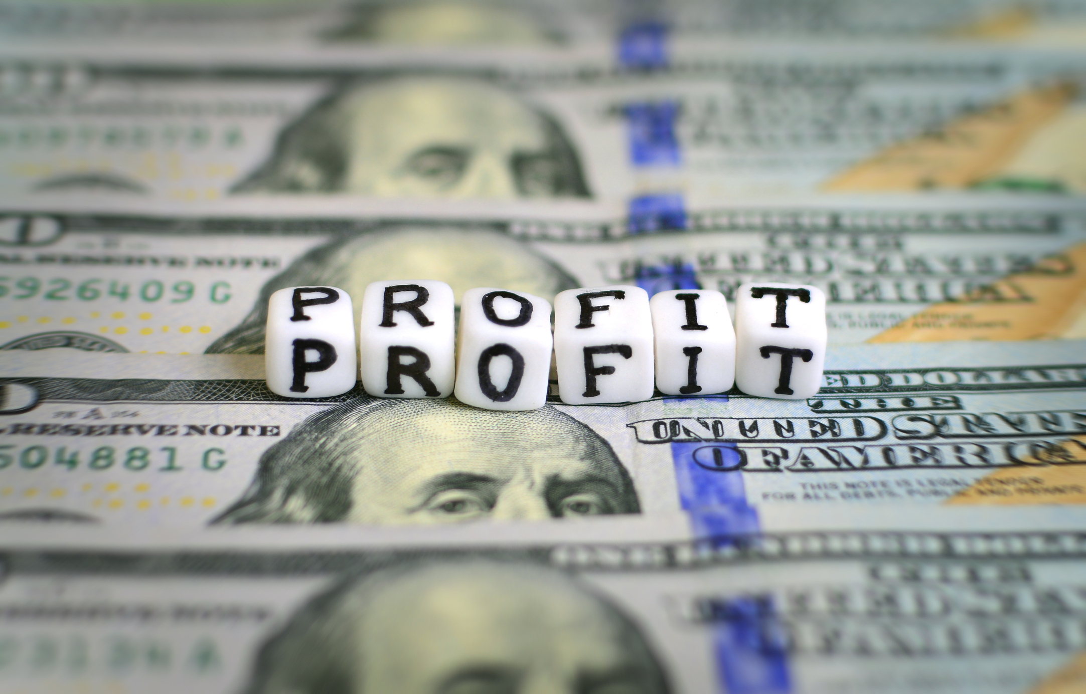 The word profit on dice-sized blocks on top of hundred-dollar bills.