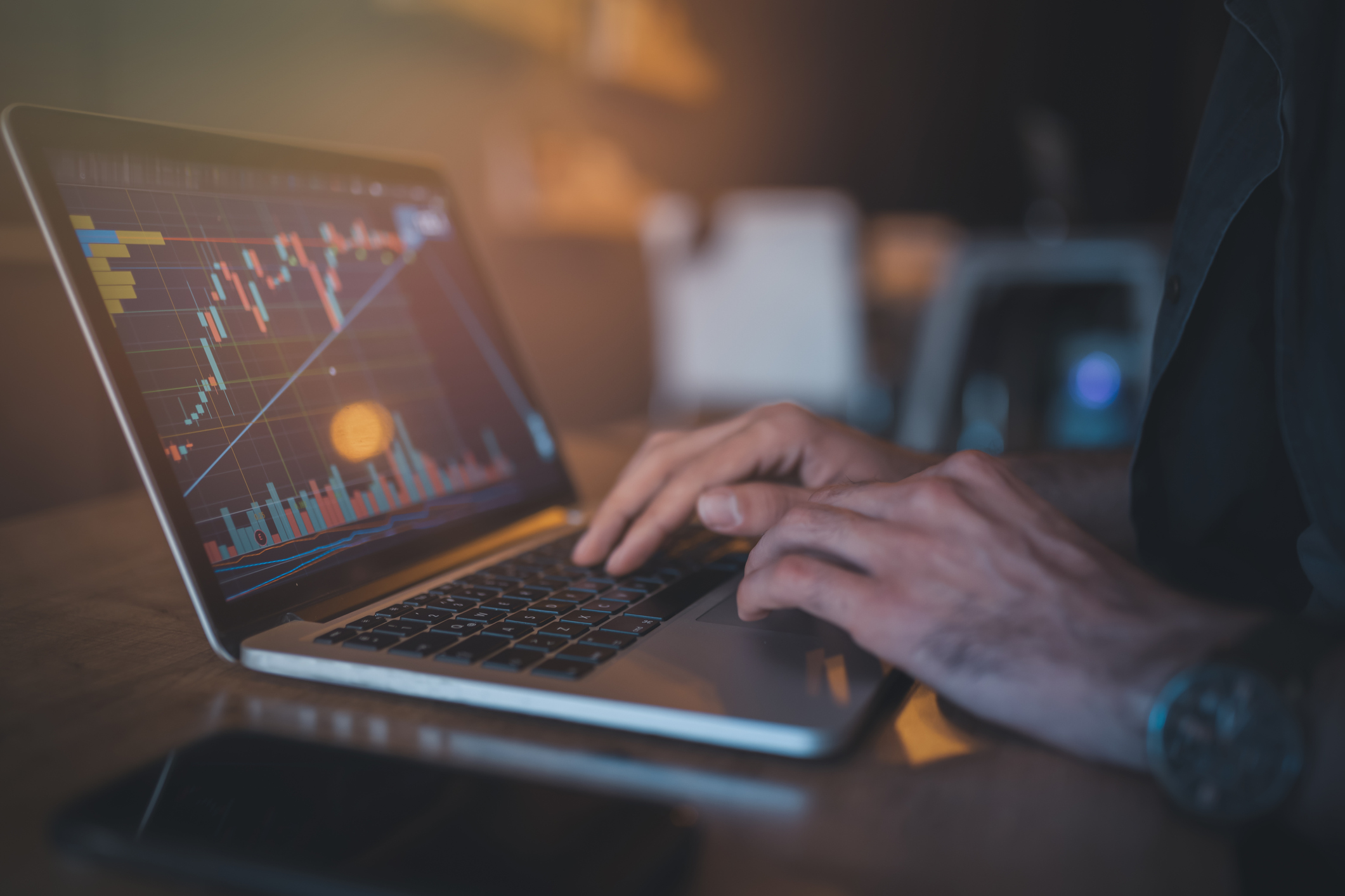 A person typing on a laptop that's displaying a rapidly rising chart with a defined trendline.