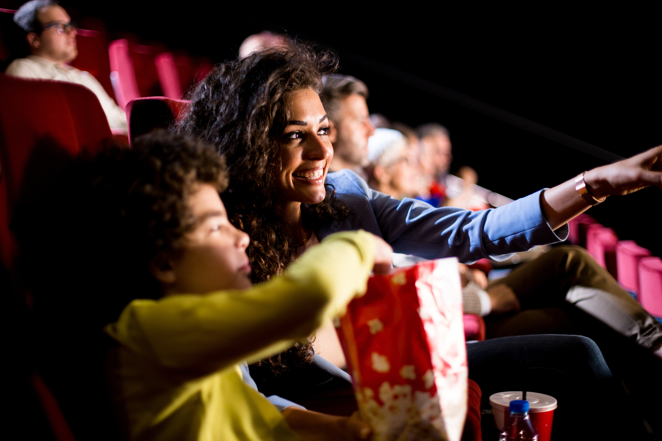 Adult and child in a movie theater eating popcorn and watching a film.