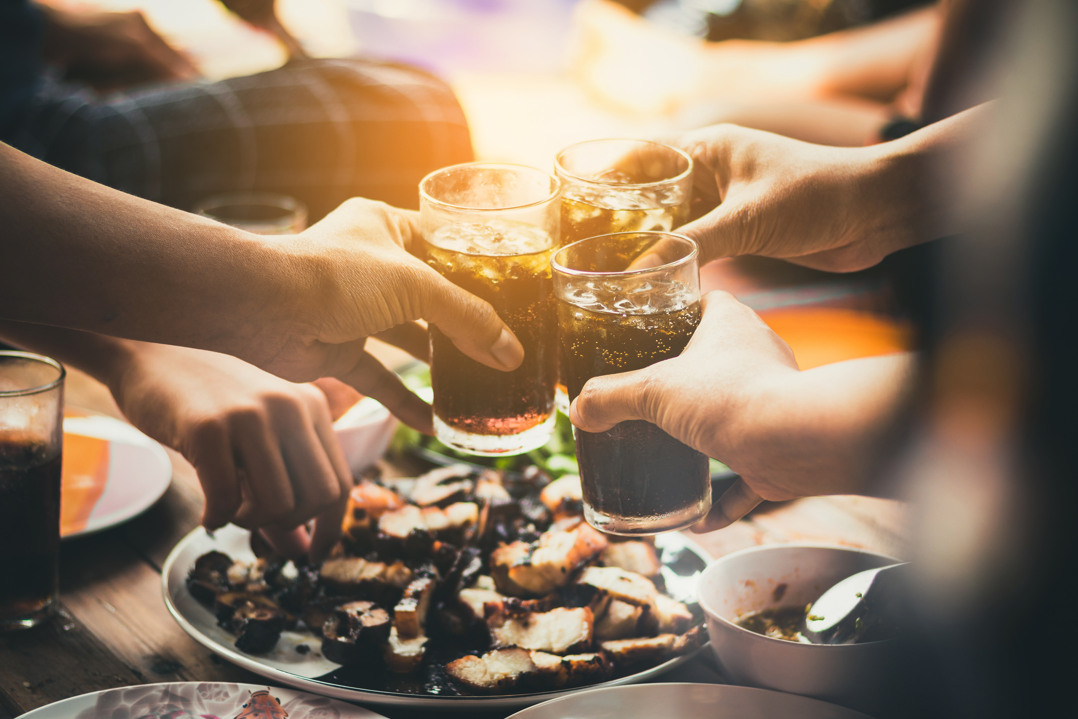 People eating and tapping their sodas together over their food.