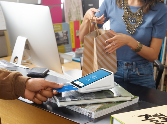 A person inserting their credit card into a Block point-of-sale card-reading device.