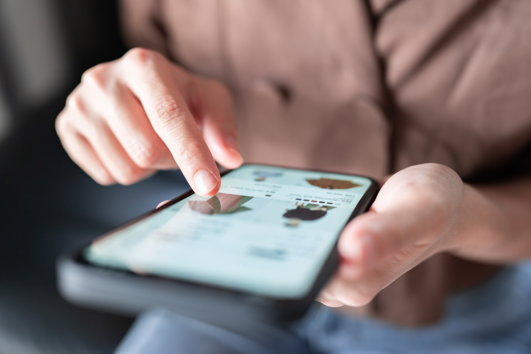 Closeup on person's hand scrolling on a phone displaying clothing.