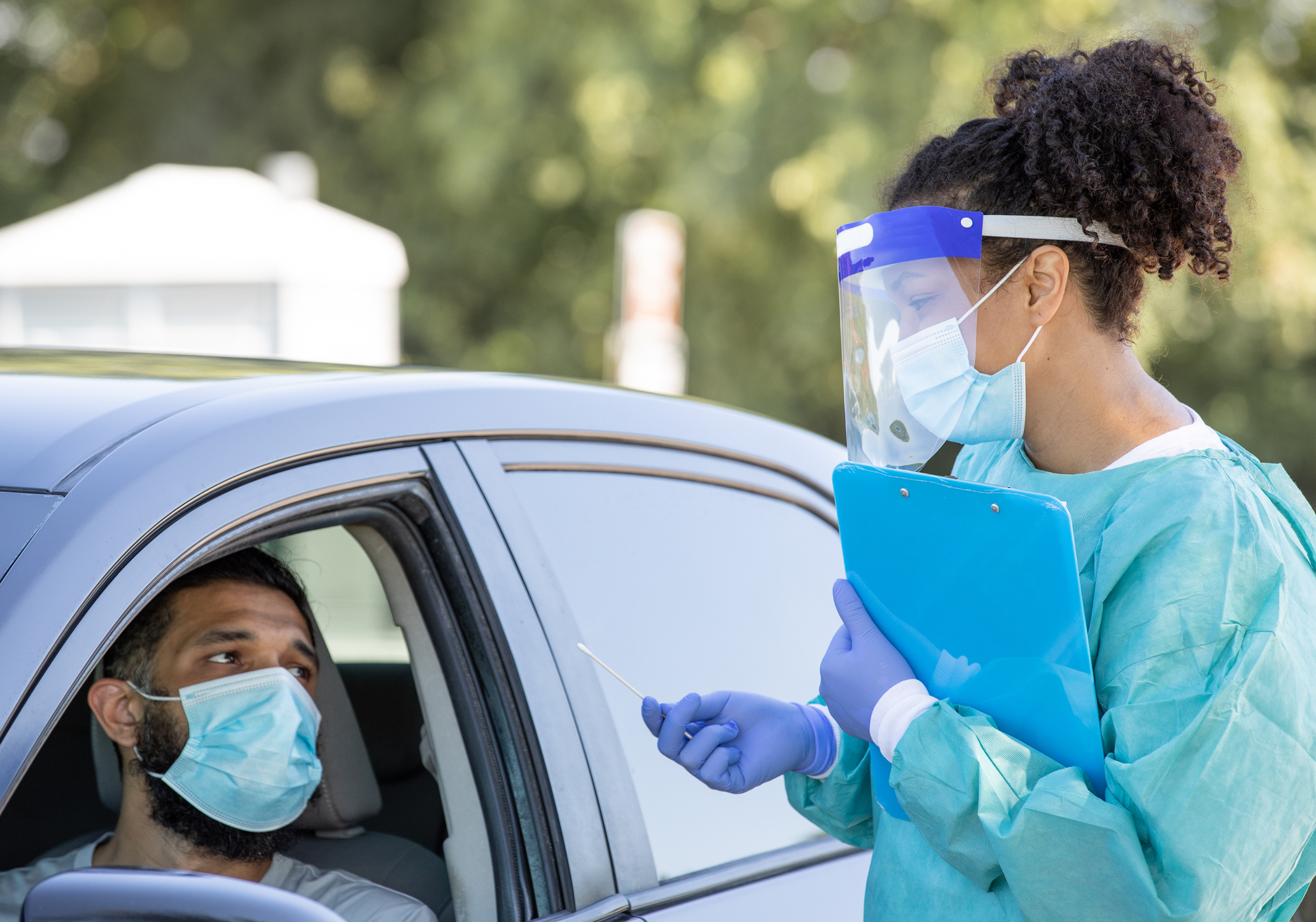 A medical technician talks with a patient in a car.