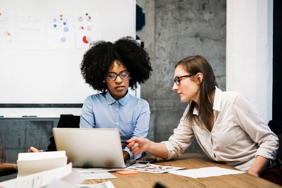 Two people using a laptop and whiteboard to discuss business strategy. 