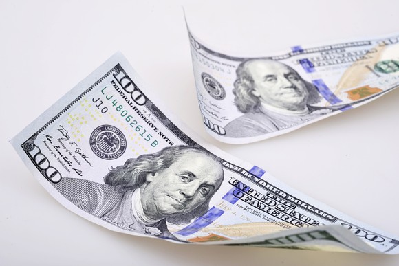 Two slightly curled one hundred dollar bills placed on a smooth surface. 