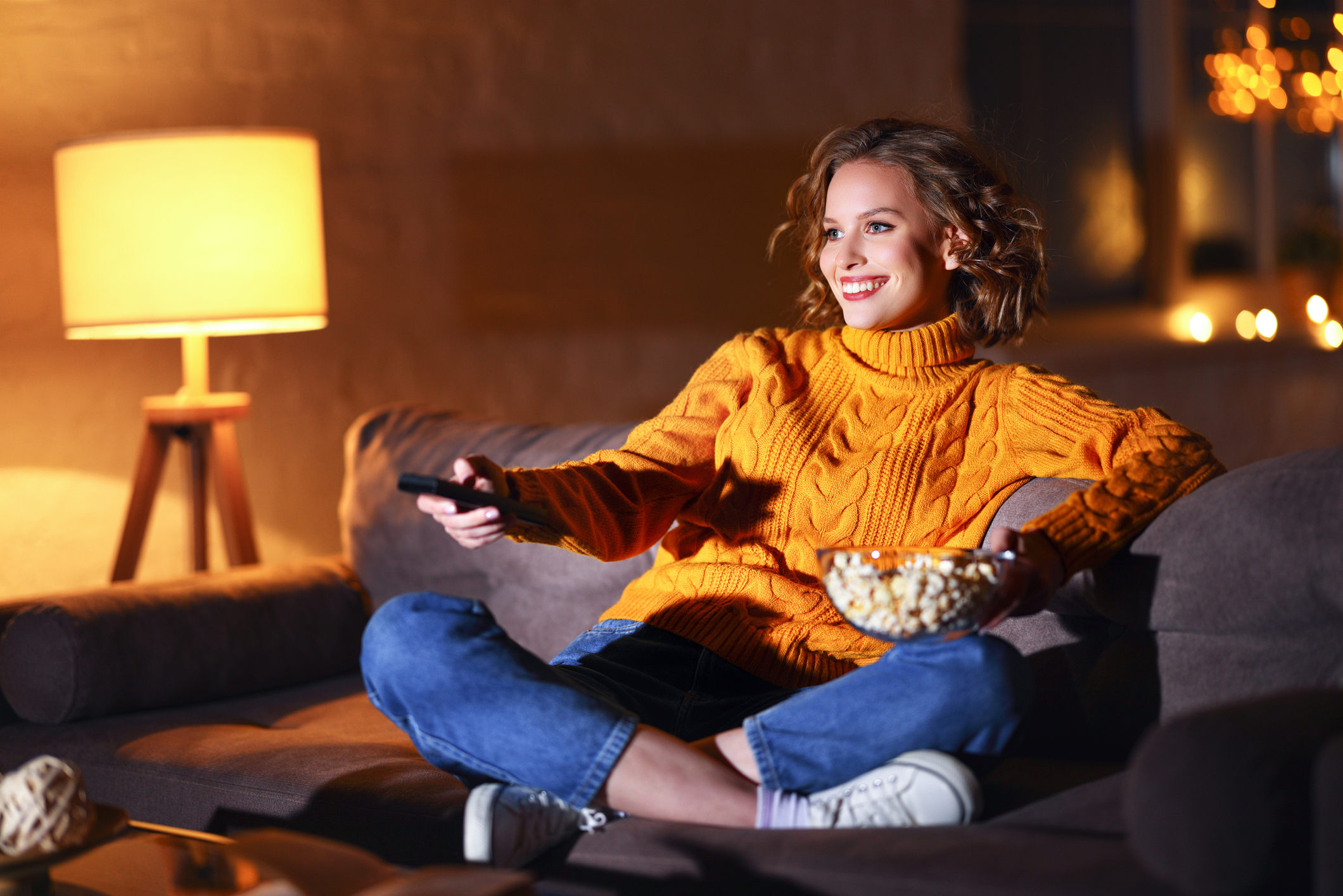 Person eating popcorn on couch and watching TV.