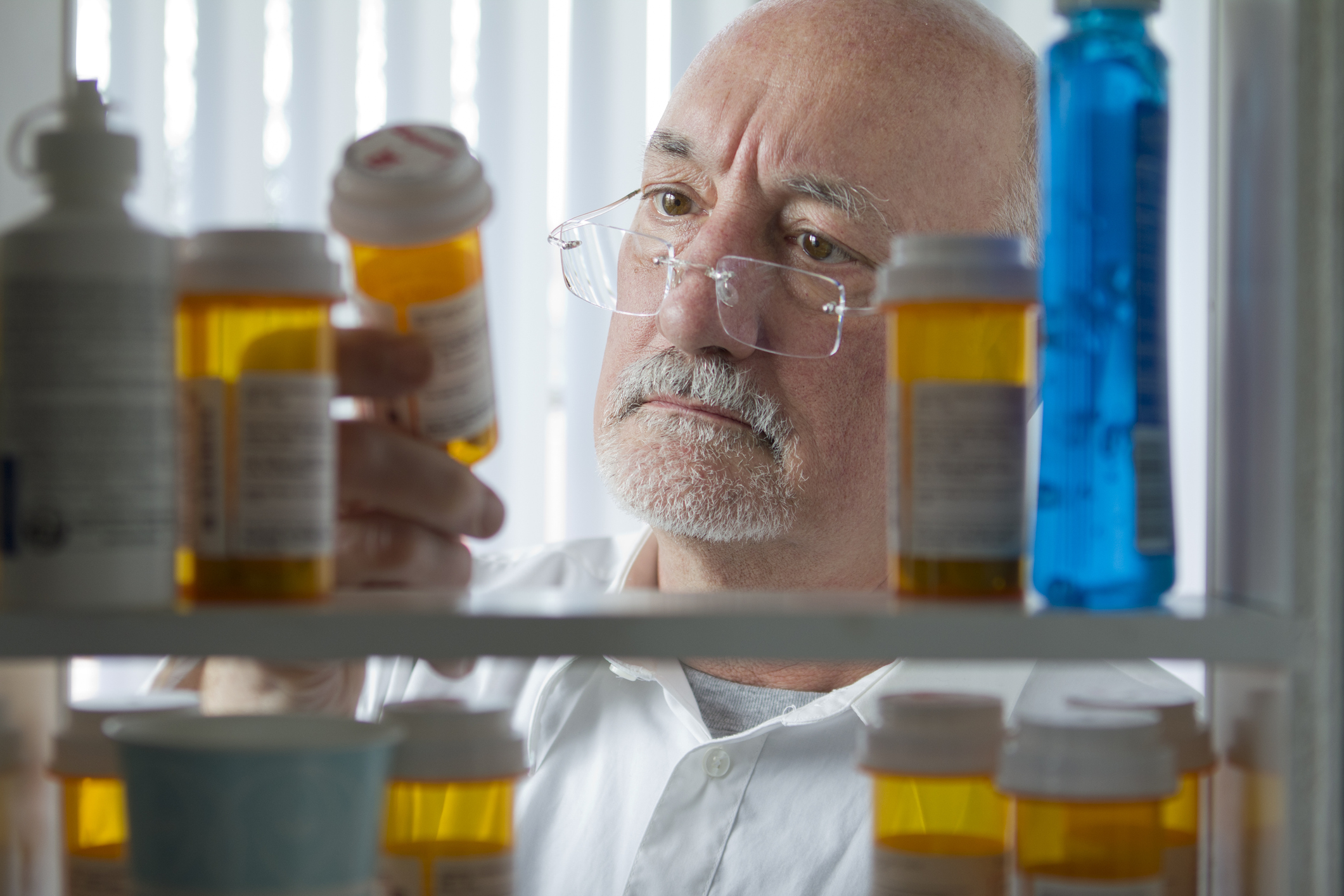 A senior citizen looking at a prescription bottle in a relatively full medicine cabinet. 