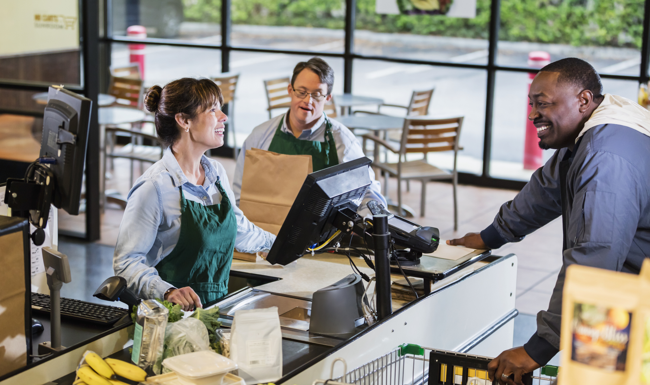 Cashier and bagger checking person out at grocery store.