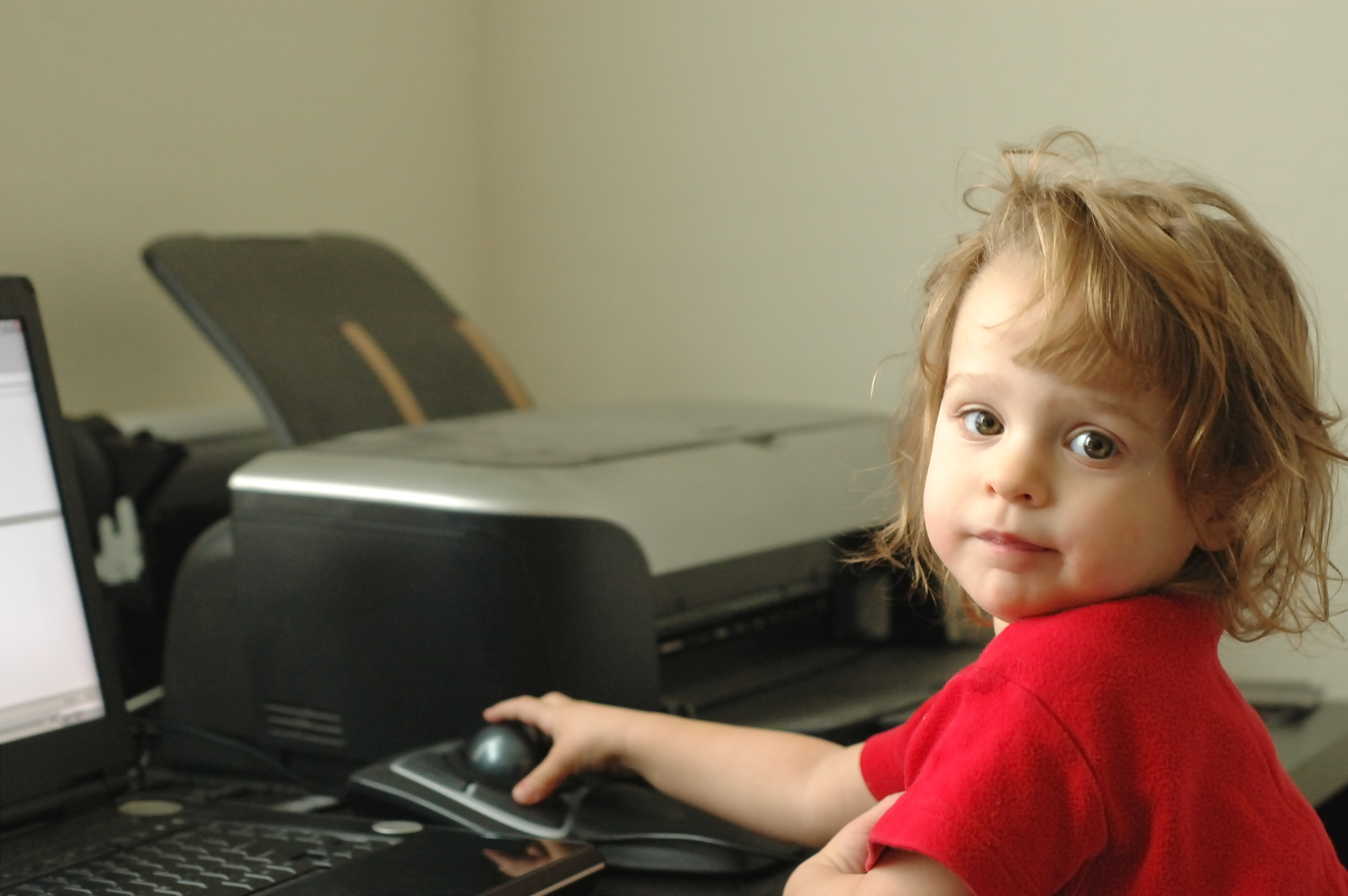 A child sitting at a computer with their hand on a trackball.