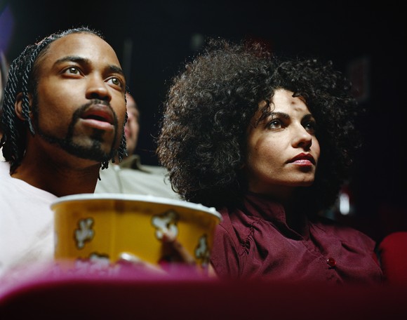 A pair of moviegoers enjoying a movie with a tub of popcorn.