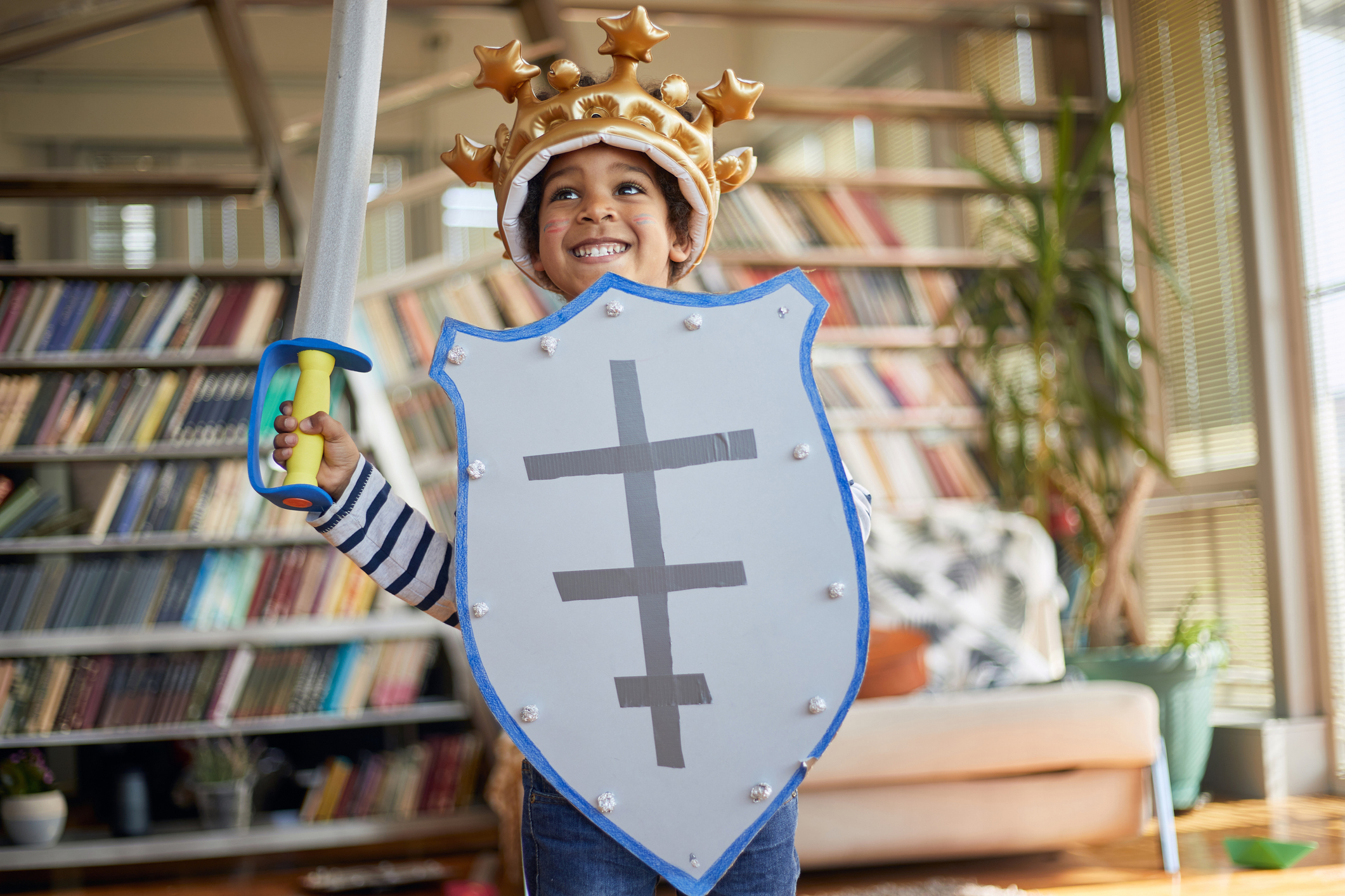 A child is smiling, sporting a crown, sword, and shield.