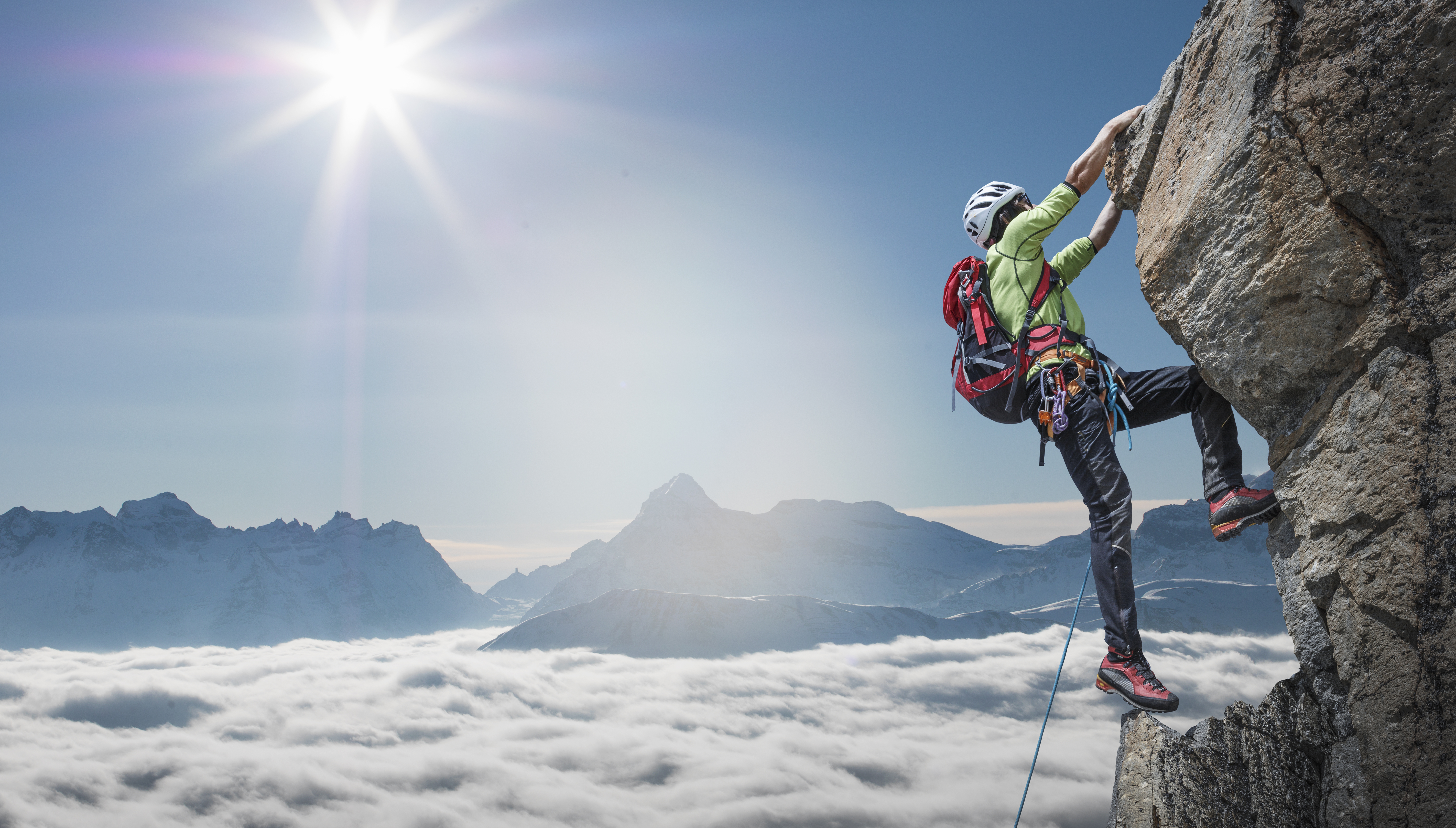 A climber clinging to rocks near the summit of a mountain, above the clouds.