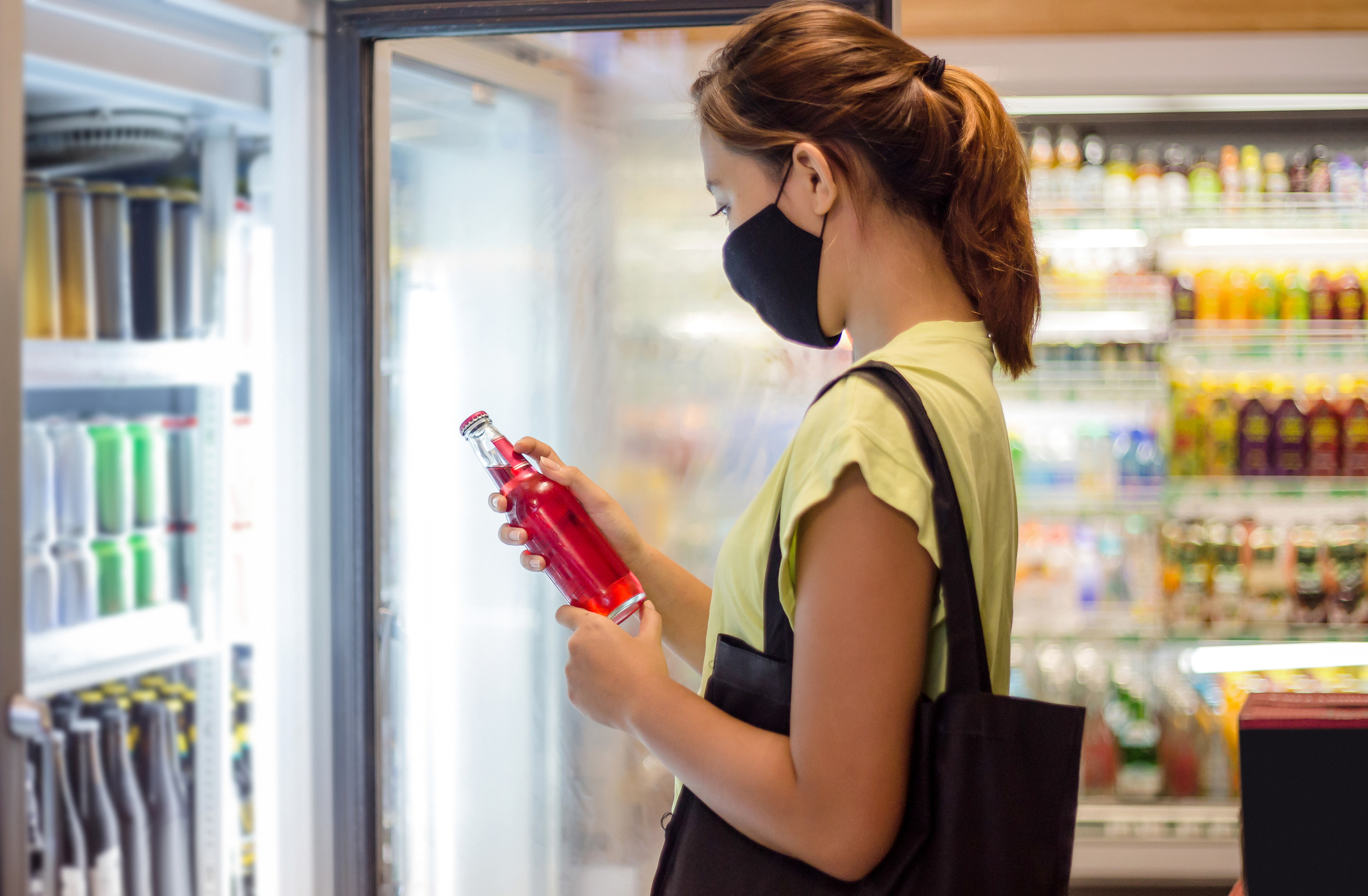 A masked person in a store holding a soda bottle_GettyImages-1269295888