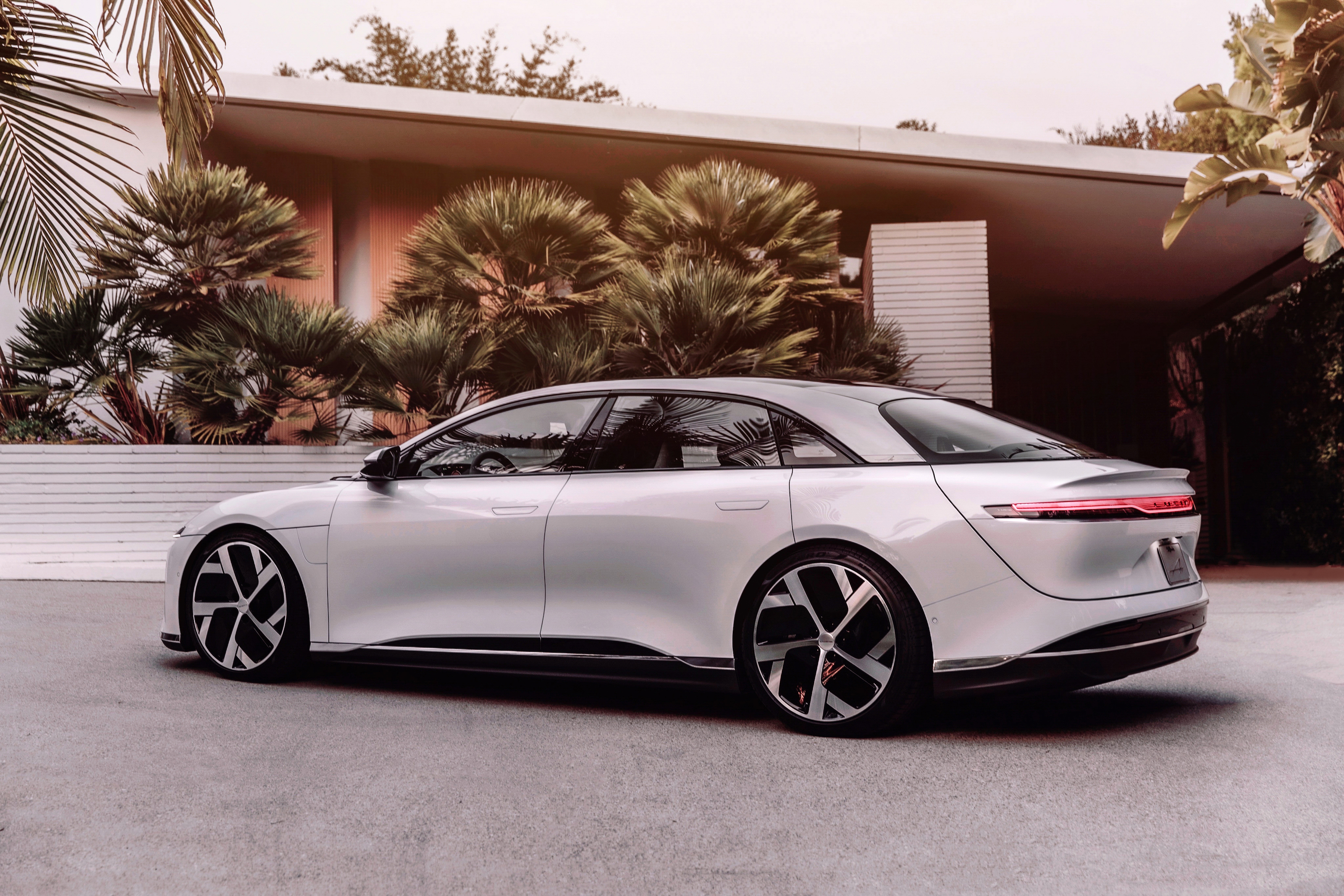 Side view of a white Lucid Air electric sedan parked in-front of a building with palm trees.