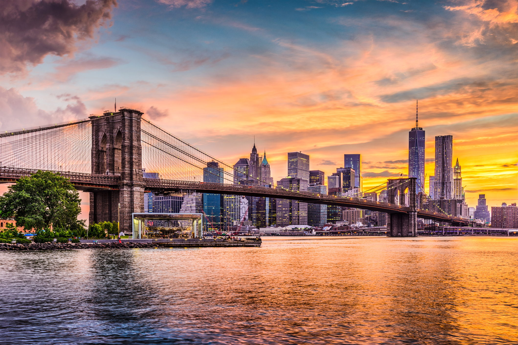 The Brooklyn Bridge with the Manhattan skyline at sunset in the background.