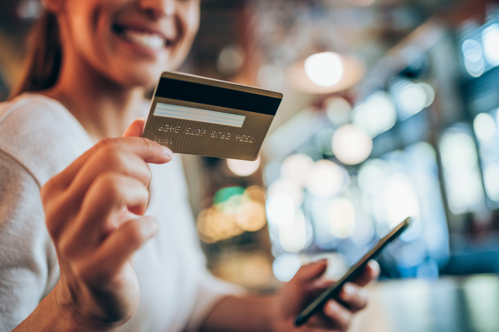 Happy person holding a payment card in one hand and a smartphone in the other.