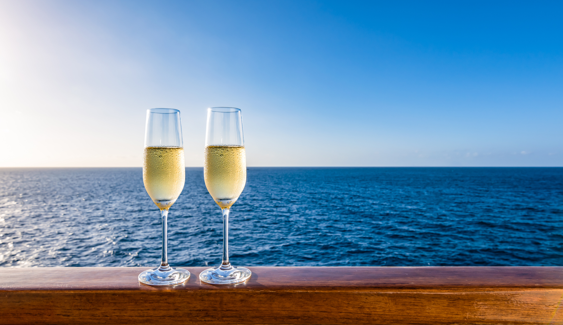 Two identical champagne glasses on the railing of a cruise ship, with a view of the ocean.