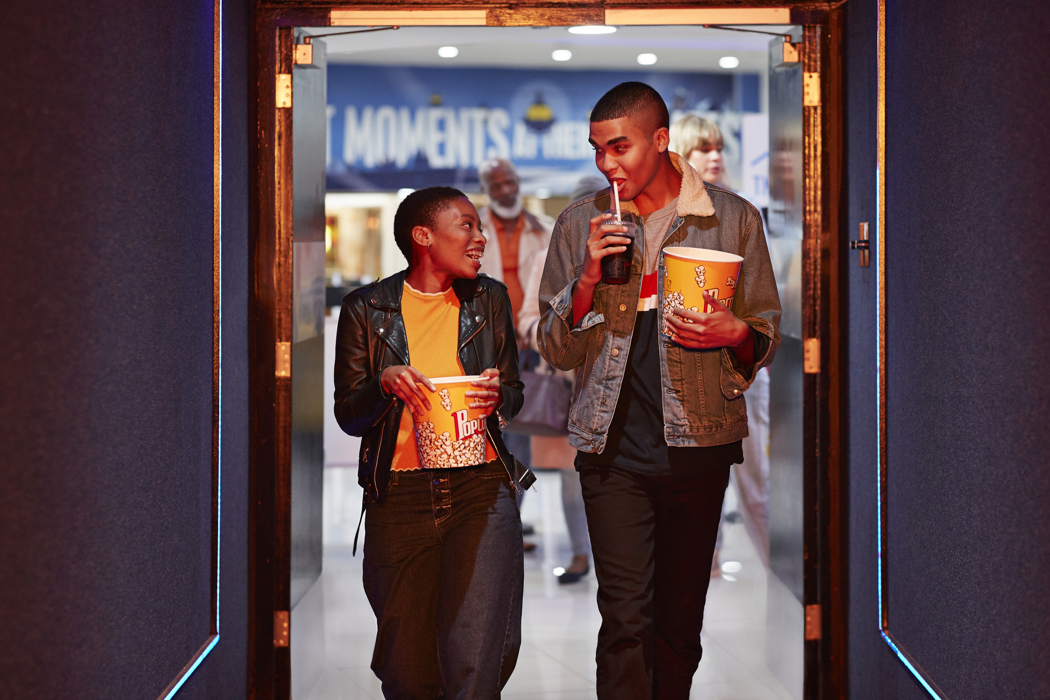 Two people walking into movie theater with popcorn from concession stand.