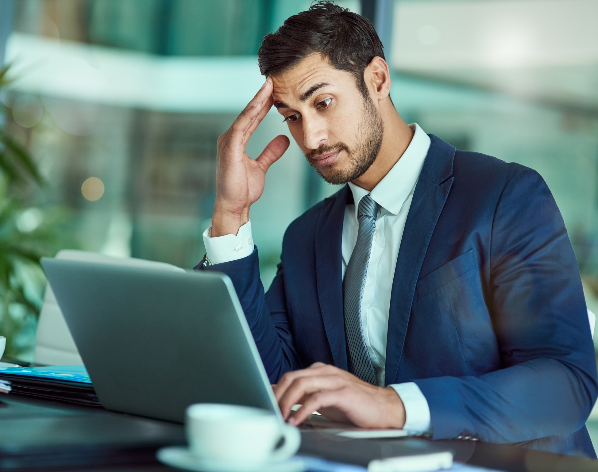 A young professional with raised eyebrows and a studious expression is working on a laptop.
