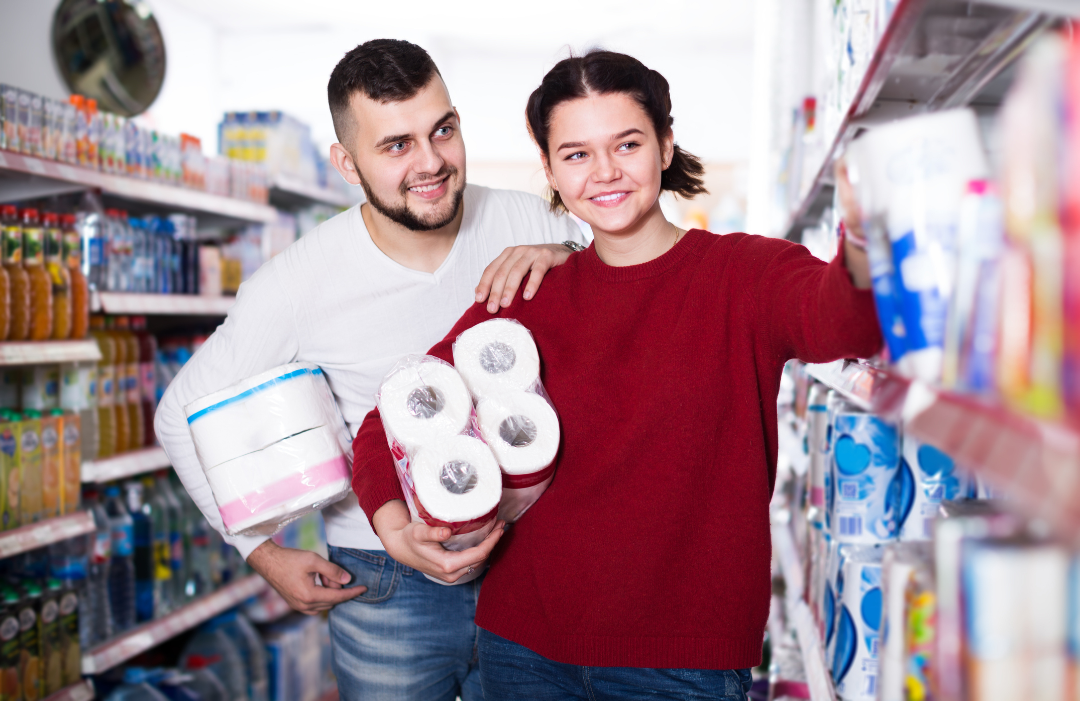 Two people smiling while shopping for paper products at grocery store.