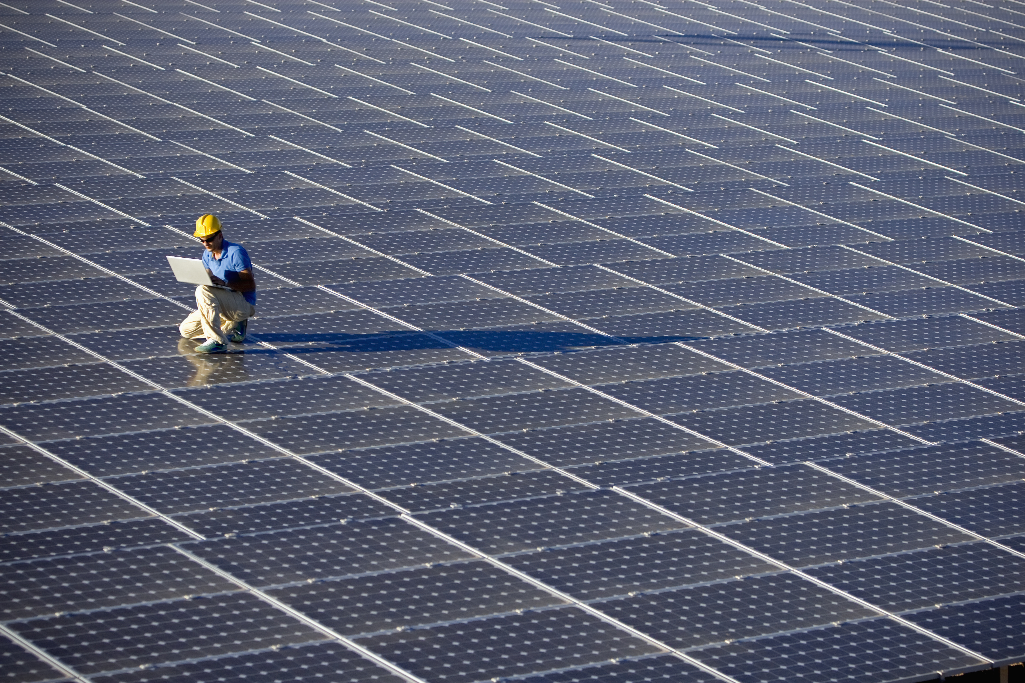 A technician on top of solar panels looking at a tablet.