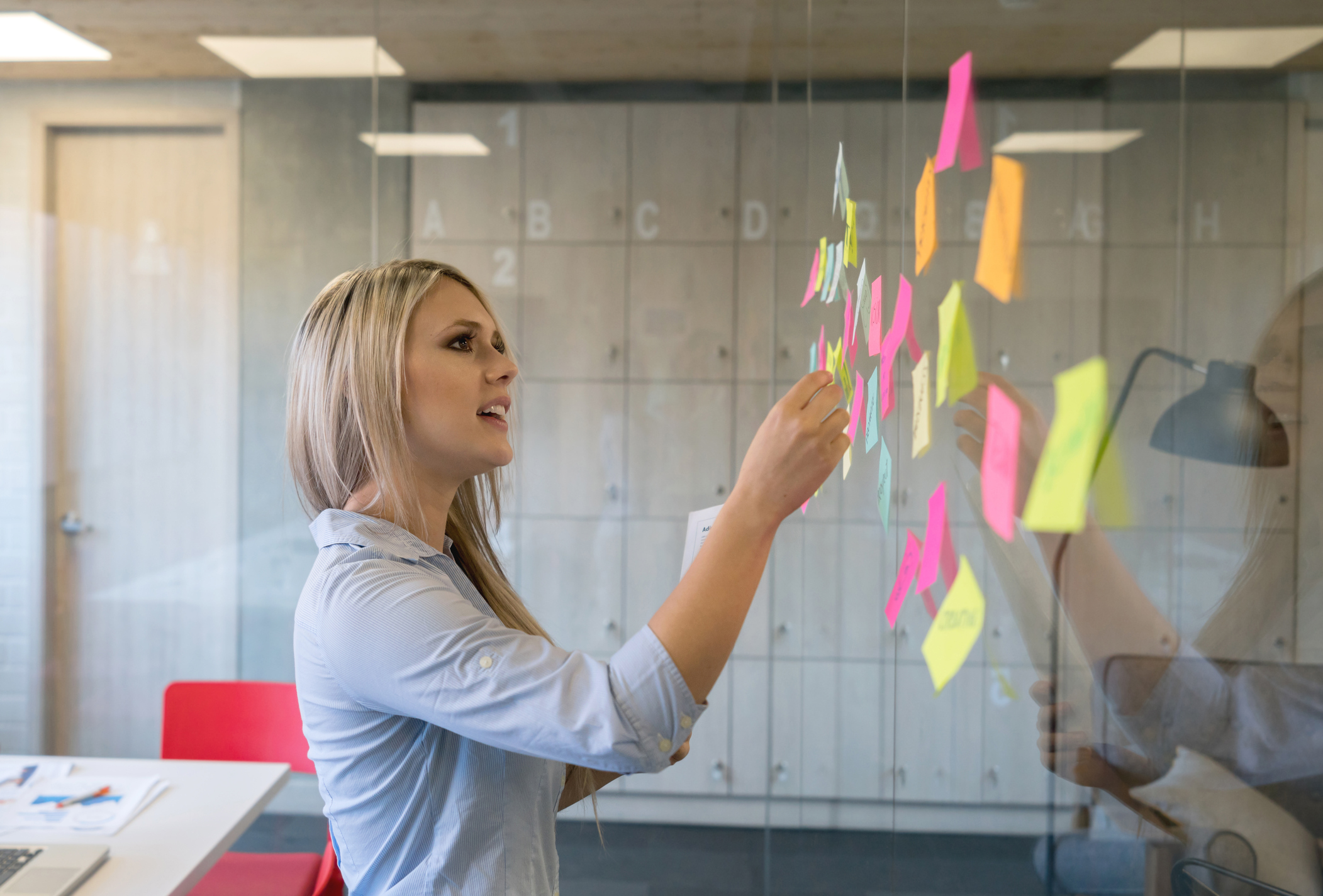 Person putting up sticky notes on a glass wall.