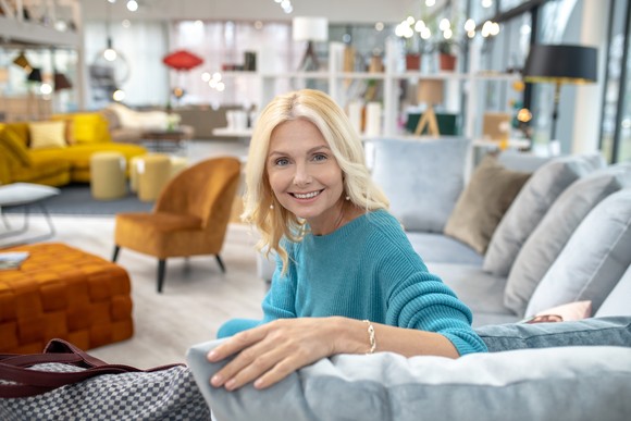A smiling person sitting on sectional couch in the middle of a furniture expo.