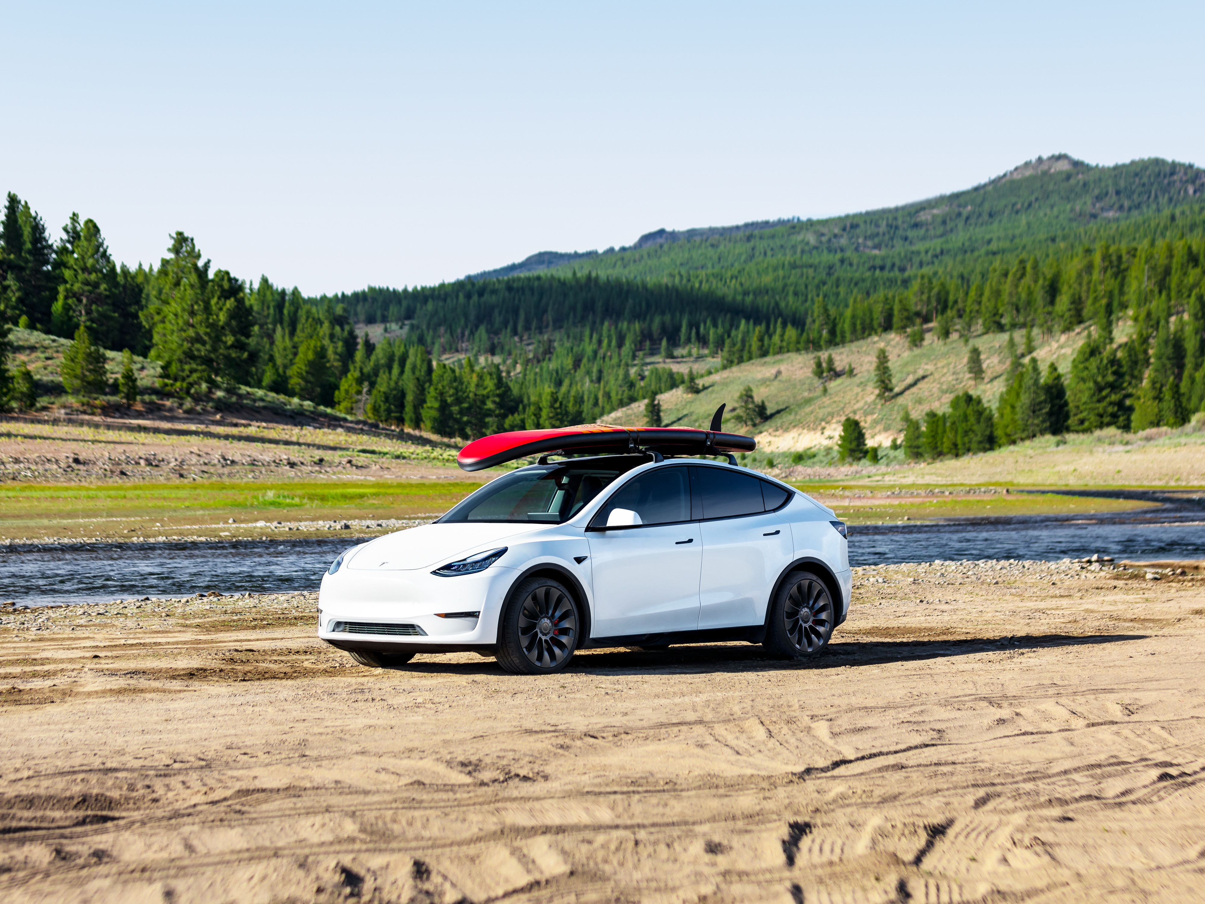 A white Tesla Model Y with surfboard on roof.