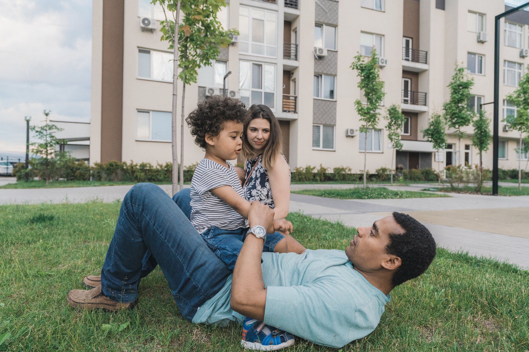 People siting in grass outside apartment community.