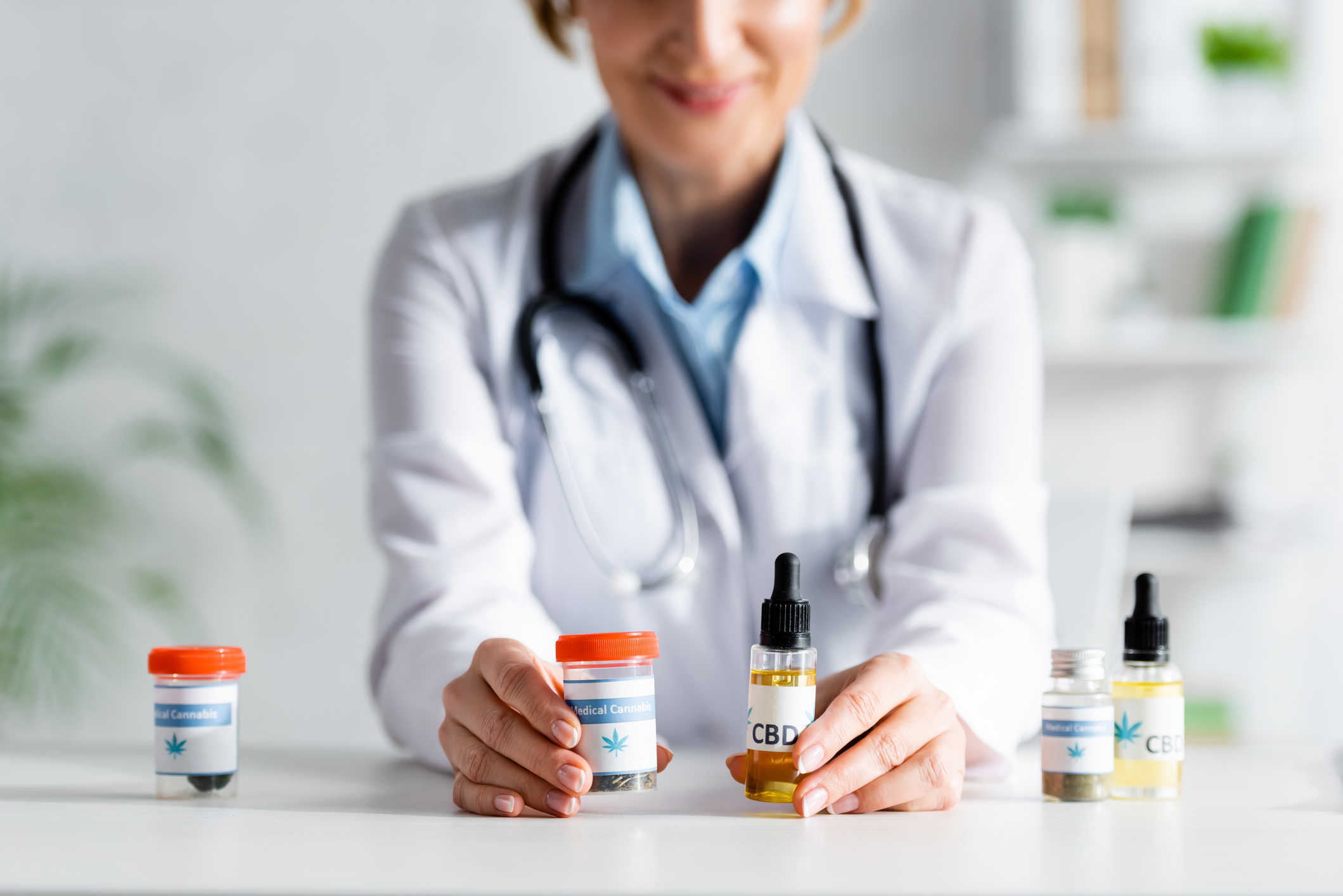 Person in lab coat holding out a bottle of oil and a bottle of medical marijuana.