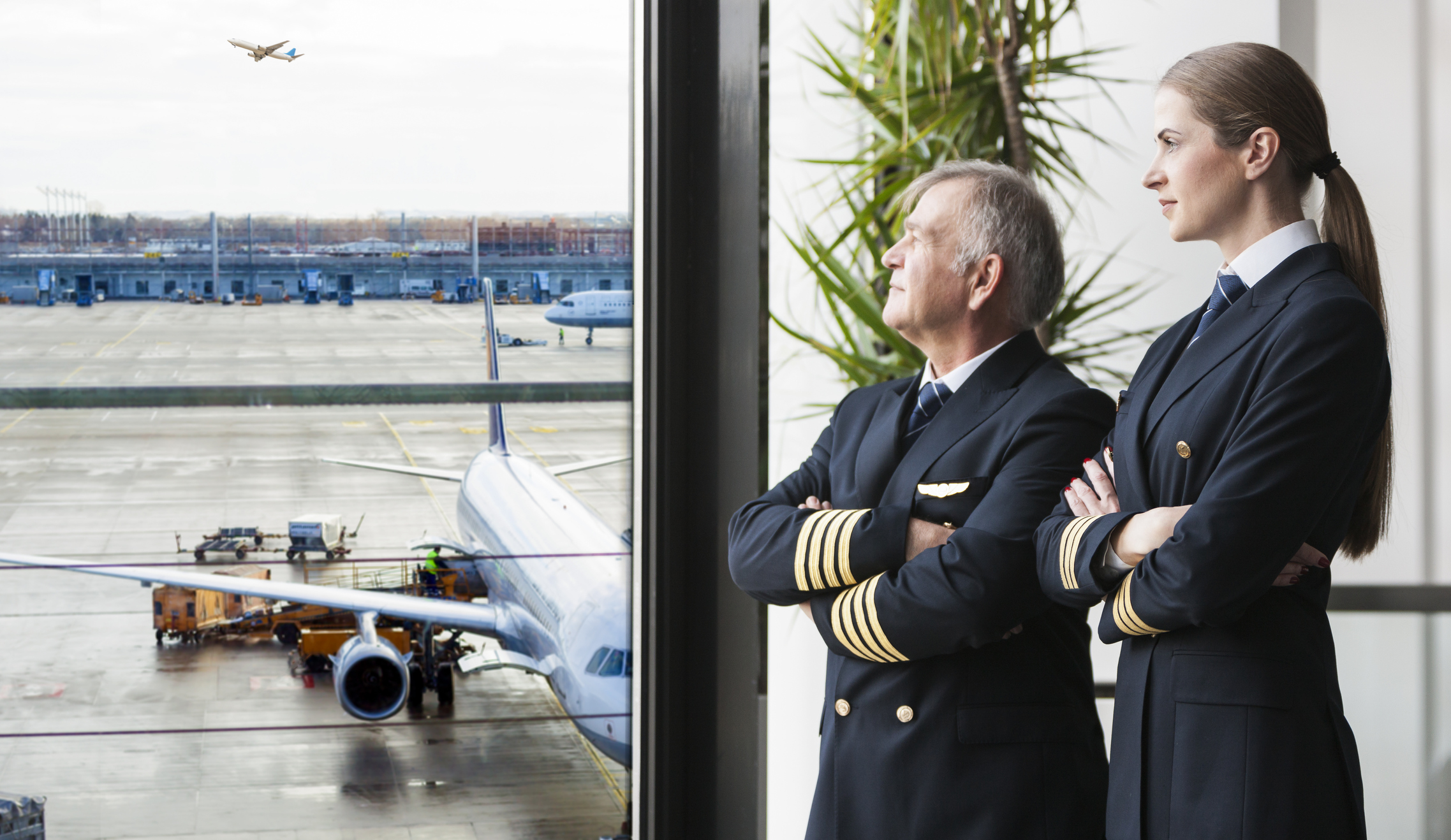 Two airline pilots looking out a window at an airport.