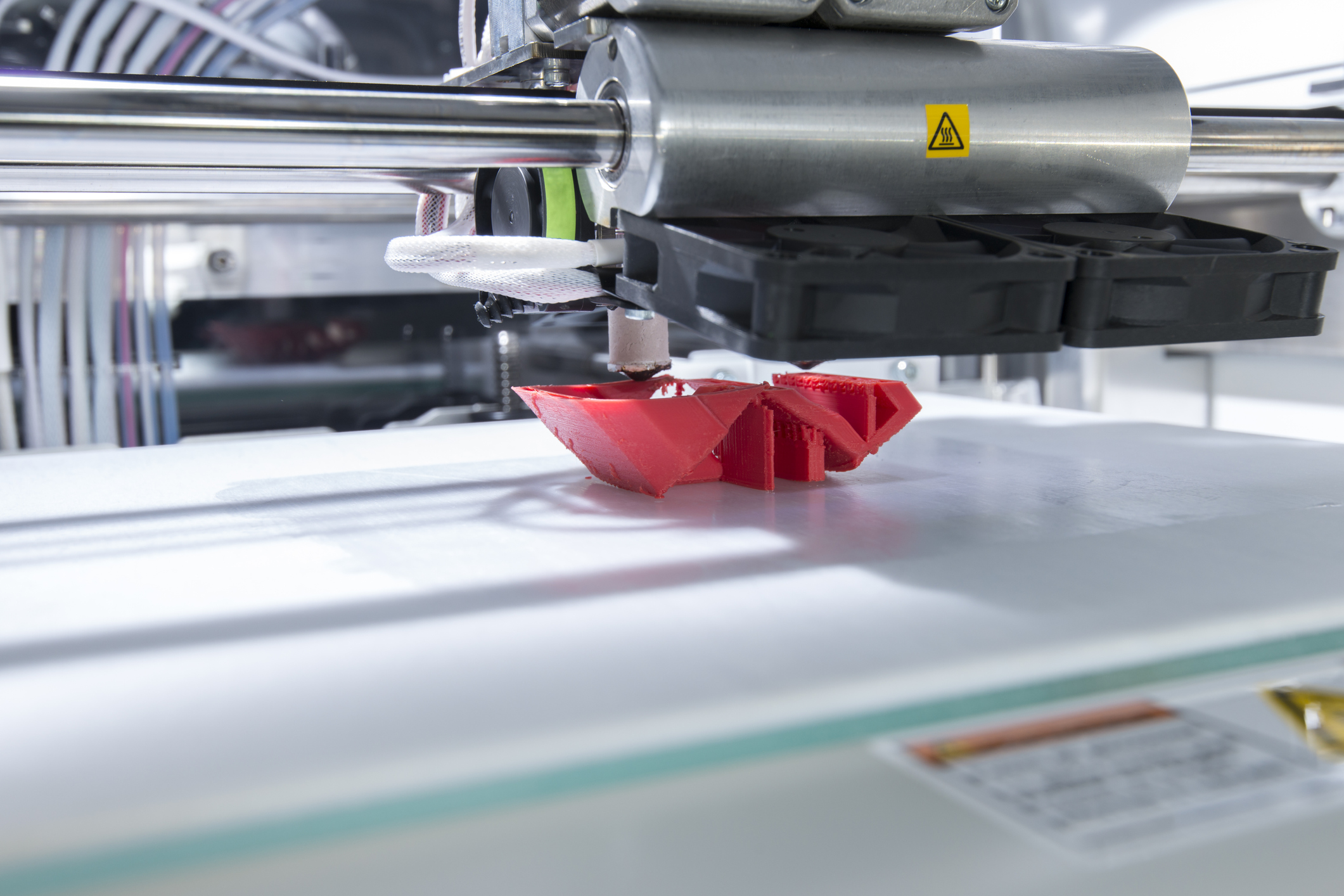 Close-up of a large, industrial 3D printer producing a red plastic object.