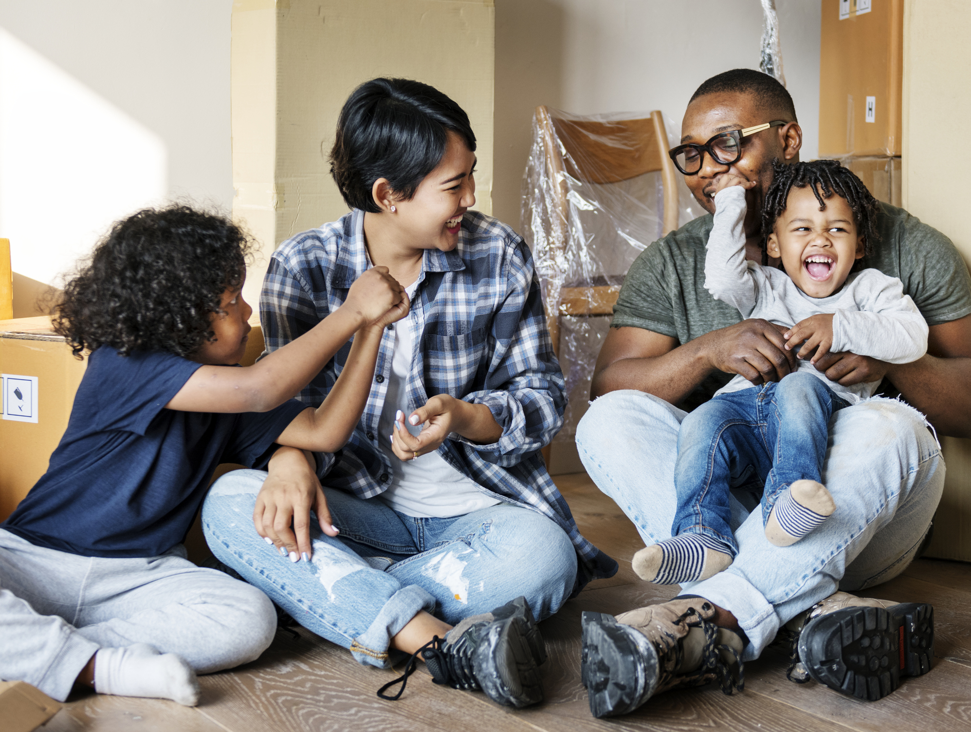 Two adults and two children in a room with packing boxes.