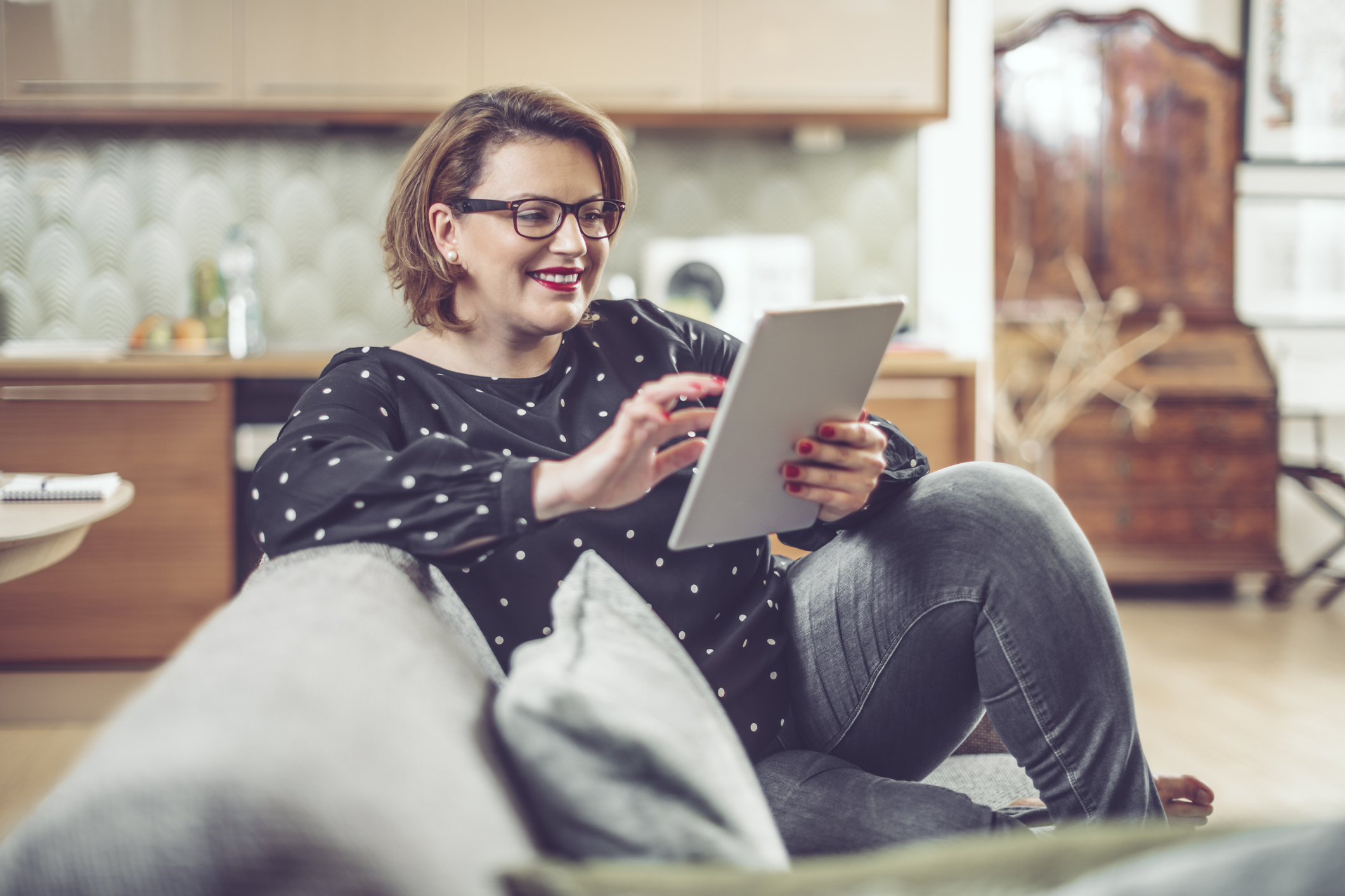 A person on couch, looking at finances on tablet, smiling.