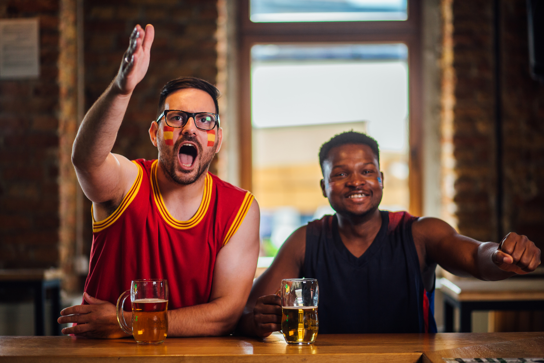 Two sports fans sitting at a bar having a beer while cheering on their respective teams